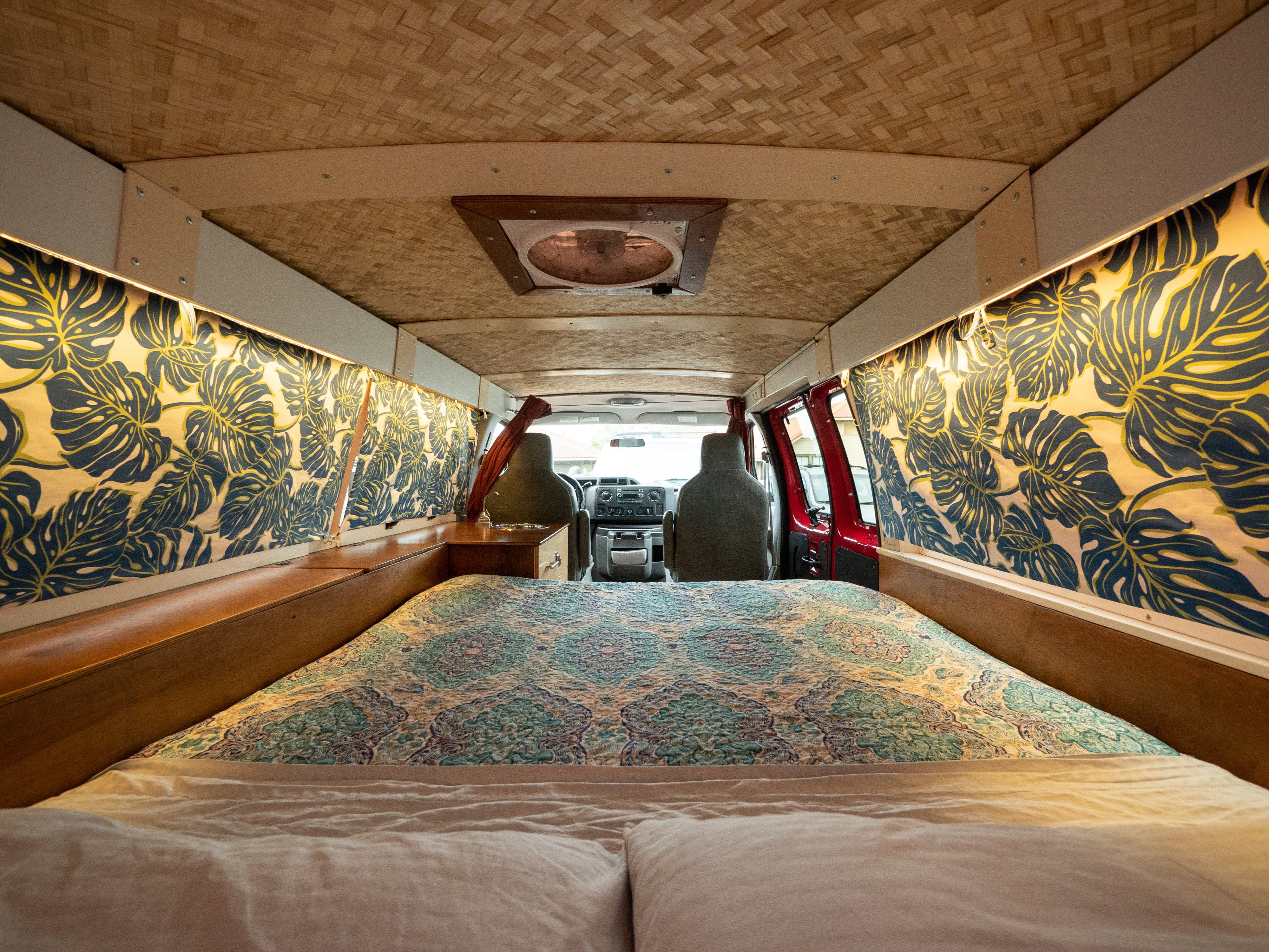 Inside this RV rental: a cozy bed with patterned quilt, tropical leaf wall decor, and a woven bamboo ceiling.. Ford E150 2011