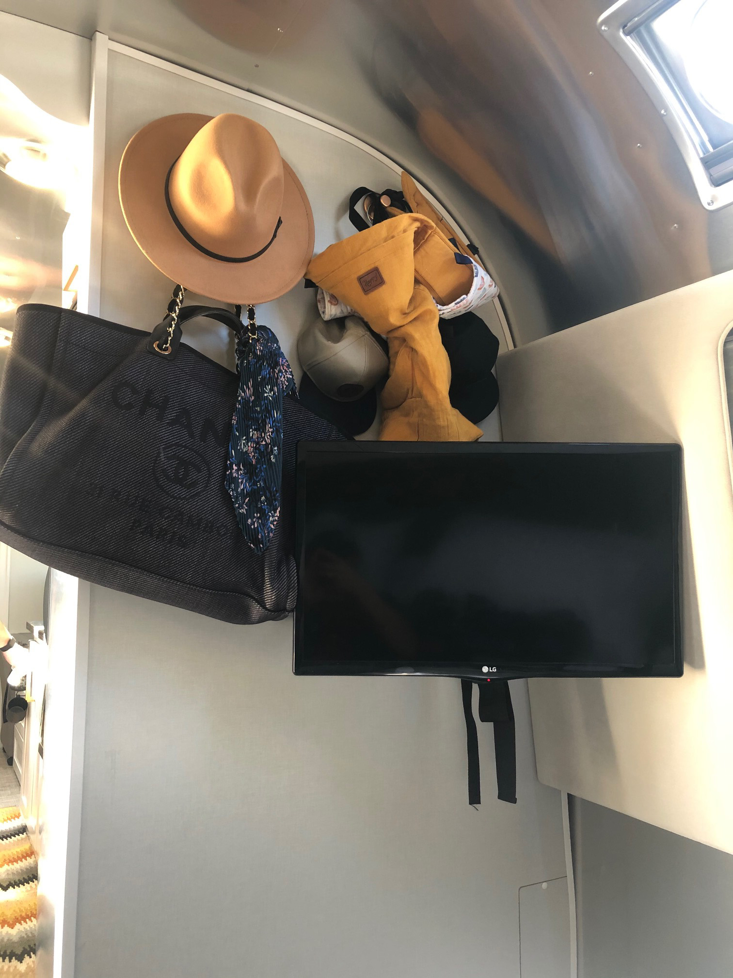 Cozy RV rental interior with organized storage: hat, designer bag, and TV visible for travel comfort.. Airstream Classic 2021