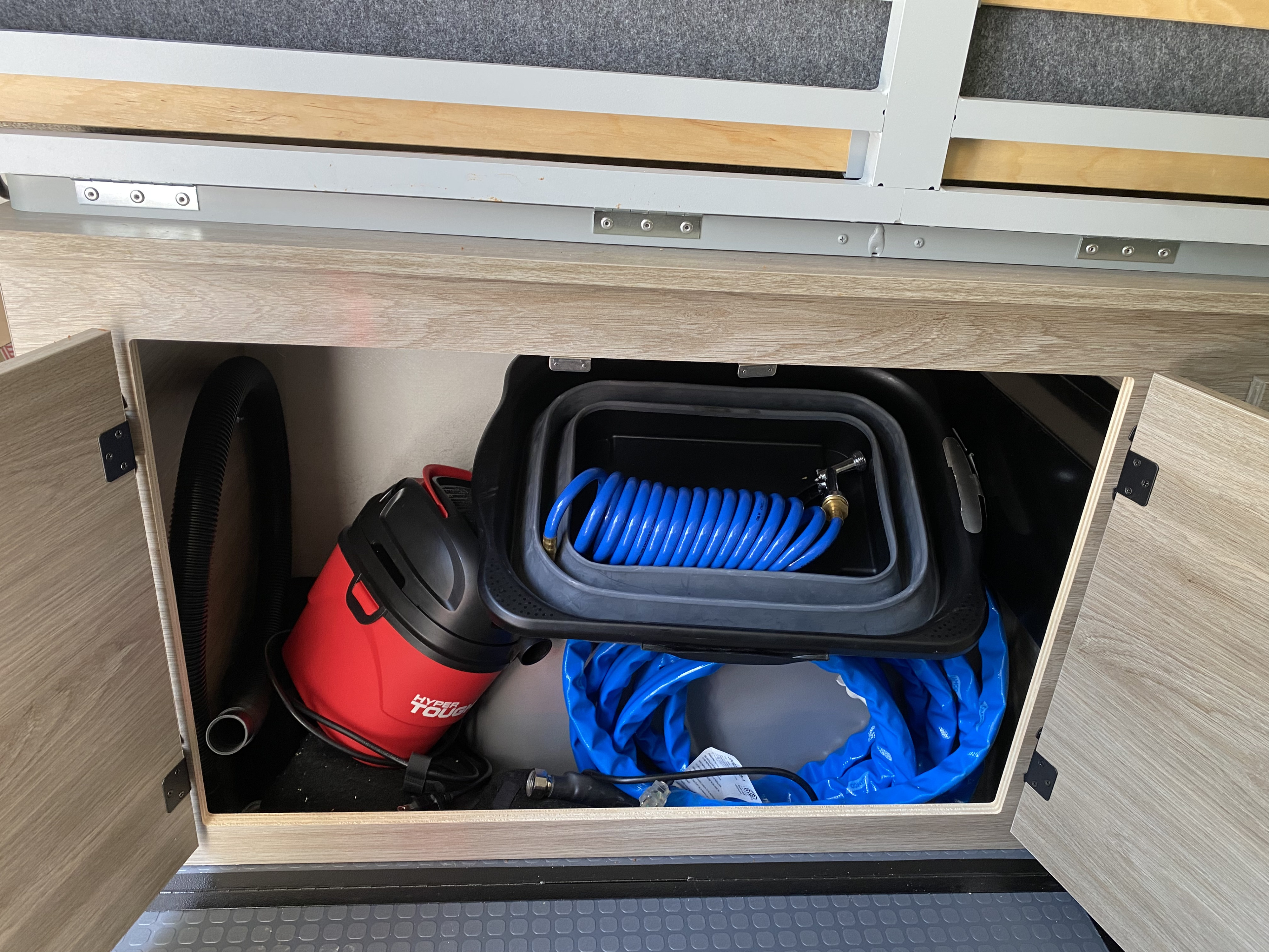 RV rental: under-bed storage revealing a red vacuum, coiled blue hoses, and a grey collapsible bucket.. Winnebago Solis 2021