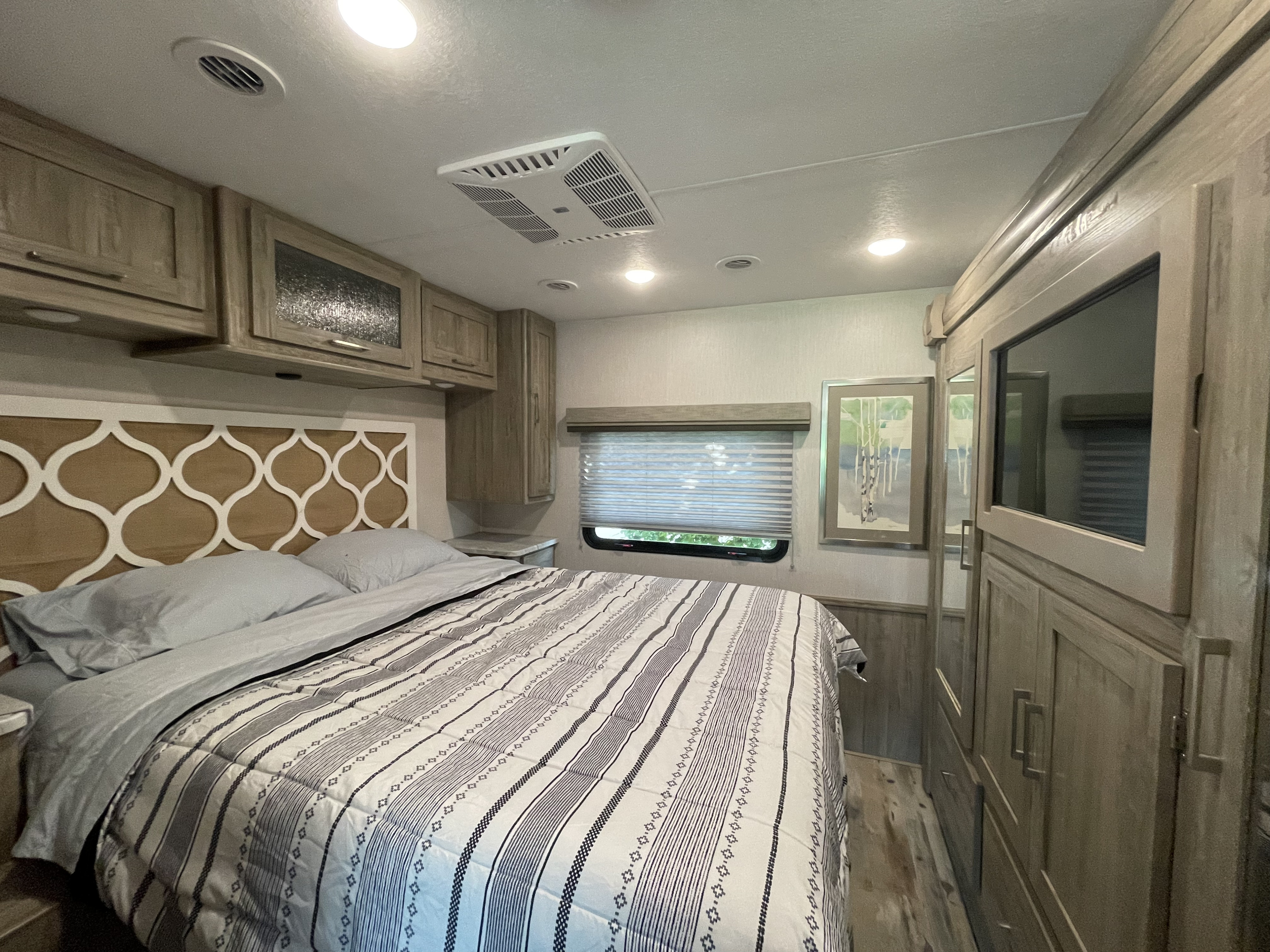 Cozy RV bedroom featuring a patterned comforter, overhead cabinets, and built-in TV. Ideal for your next RV rental.. Coachmen Pursuit 2021