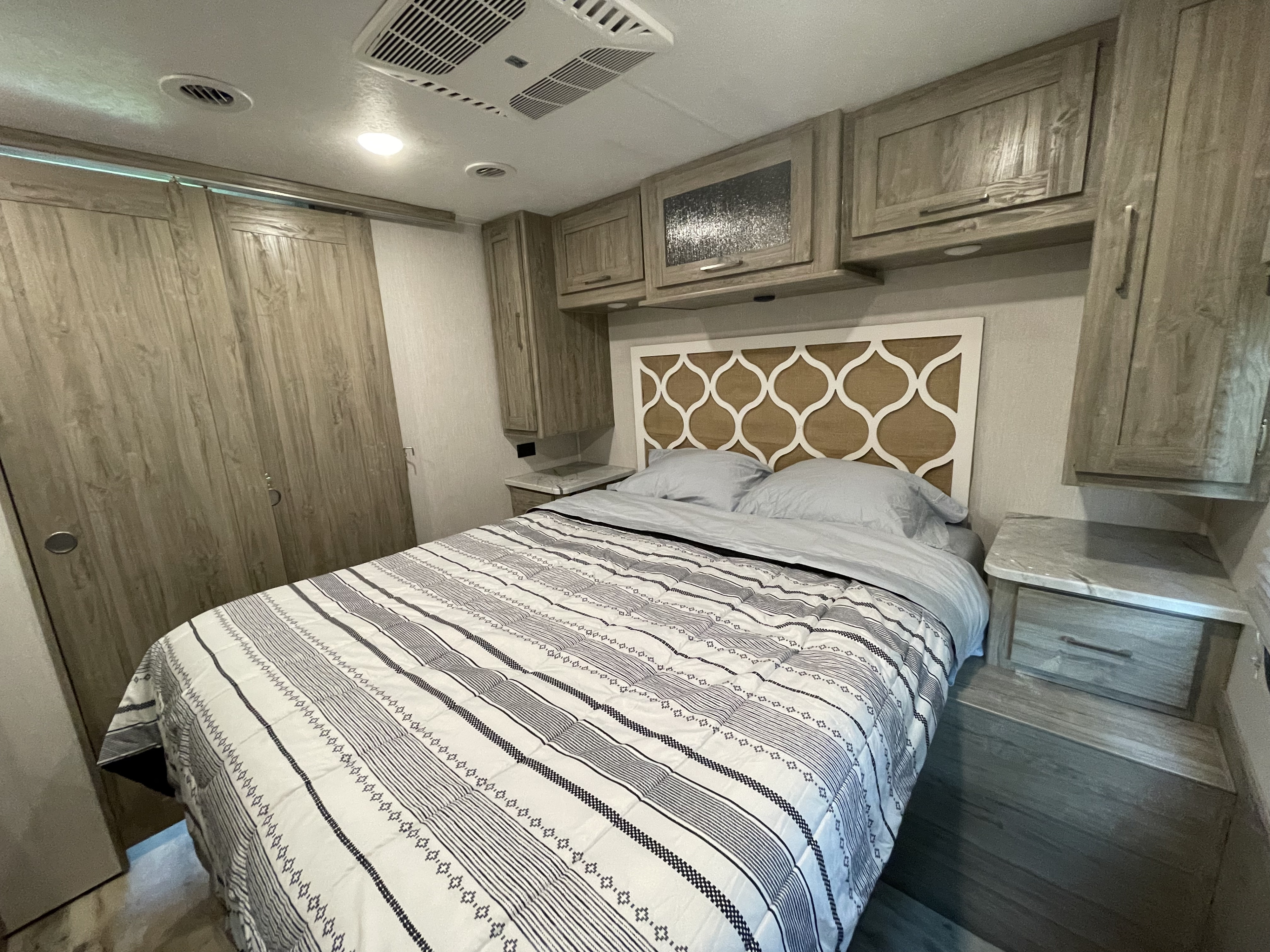 Cozy RV rental bedroom with patterned comforter, overhead storage, and wardrobe.. Coachmen Pursuit 2021