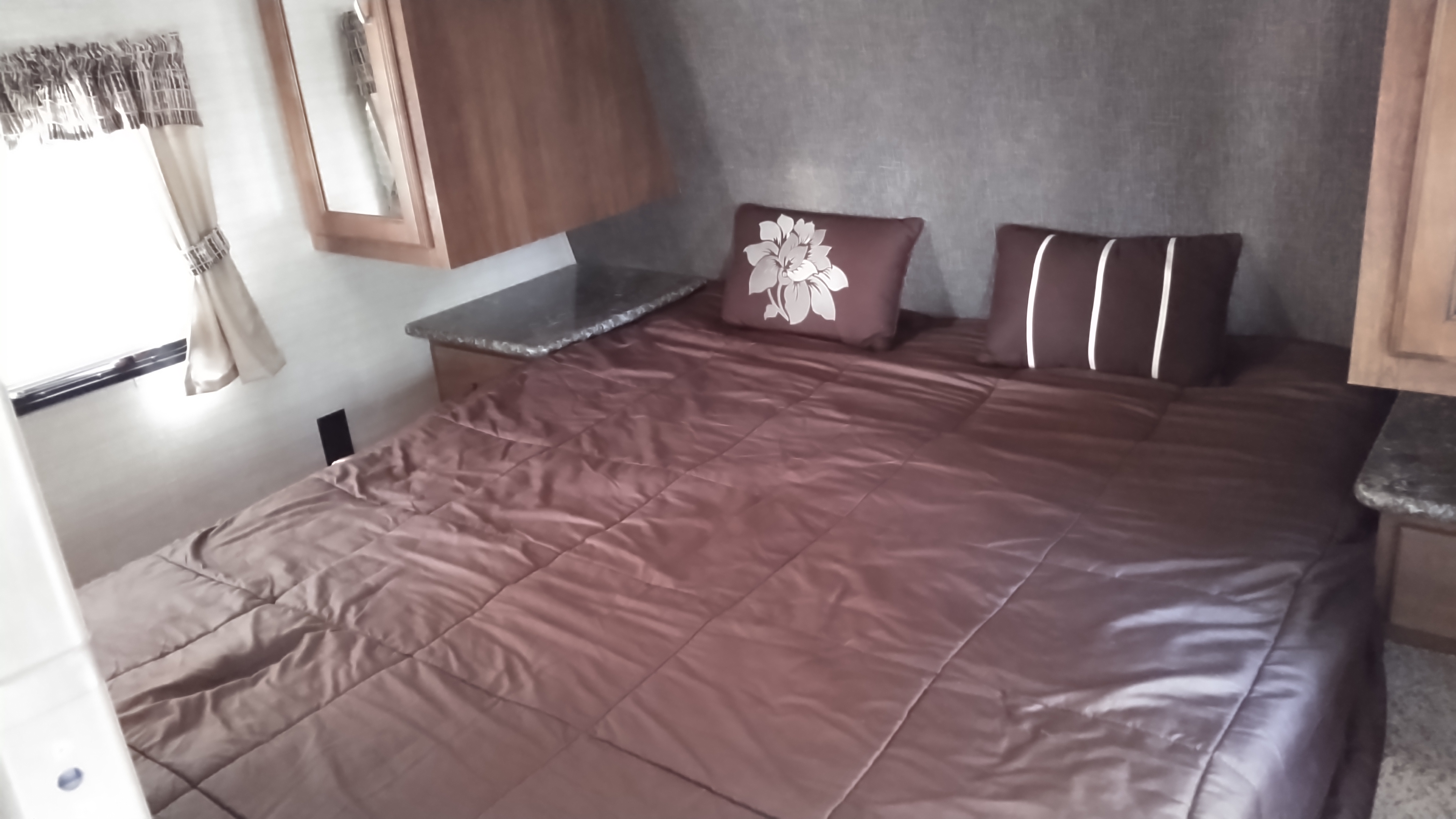 This RV rental bedroom features a large brown bed with floral and striped pillows, plus bedside storage. Ideal for comfortable travel.. Keystone Springdale 2016