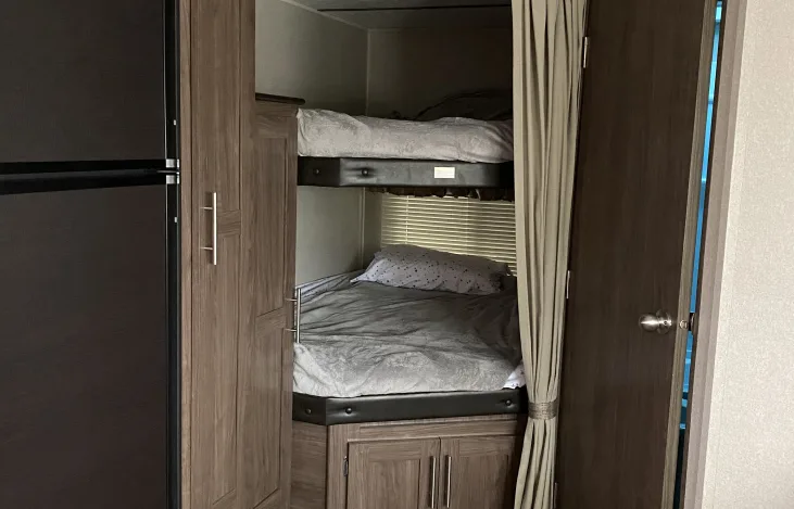View inside an RV rental: two neatly made bunk beds, a dark fridge, and wooden storage for convenience.. Keystone Hideout 2019