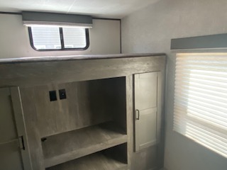 RV rental bunk room with a top bed, lower storage/entertainment area, and cabinets, well-lit by windows.. Heartland North Trail 2020