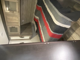 This RV rental bedroom features a bed with a vibrant striped comforter, surrounded by modern storage cabinets and wood-look flooring.. Heartland North Trail 2020