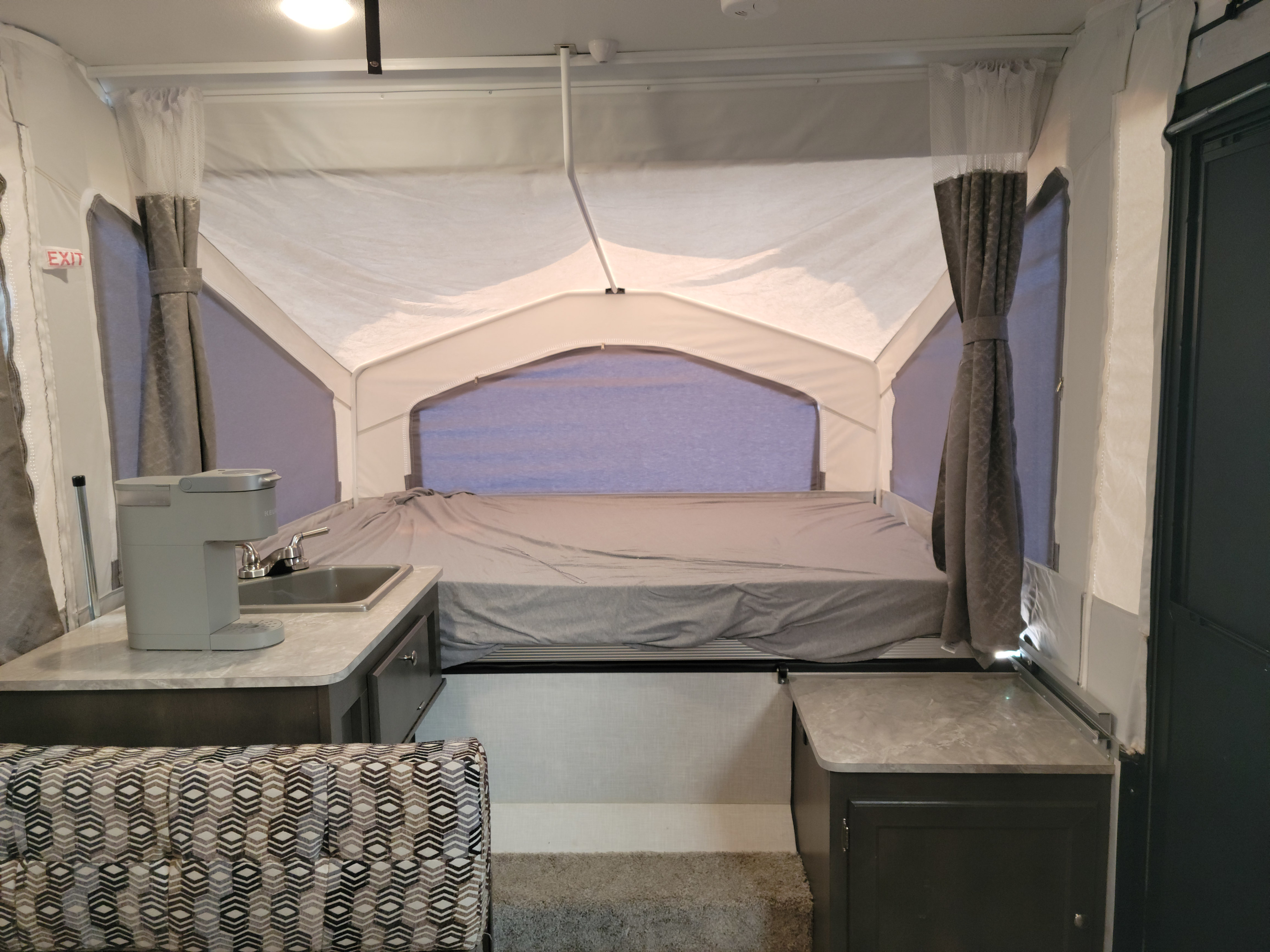 Spacious pop-up camper interior for RV rental: comfortable bed, kitchen sink with coffee maker, and patterned dinette.. Forest River Flagstaff 2021