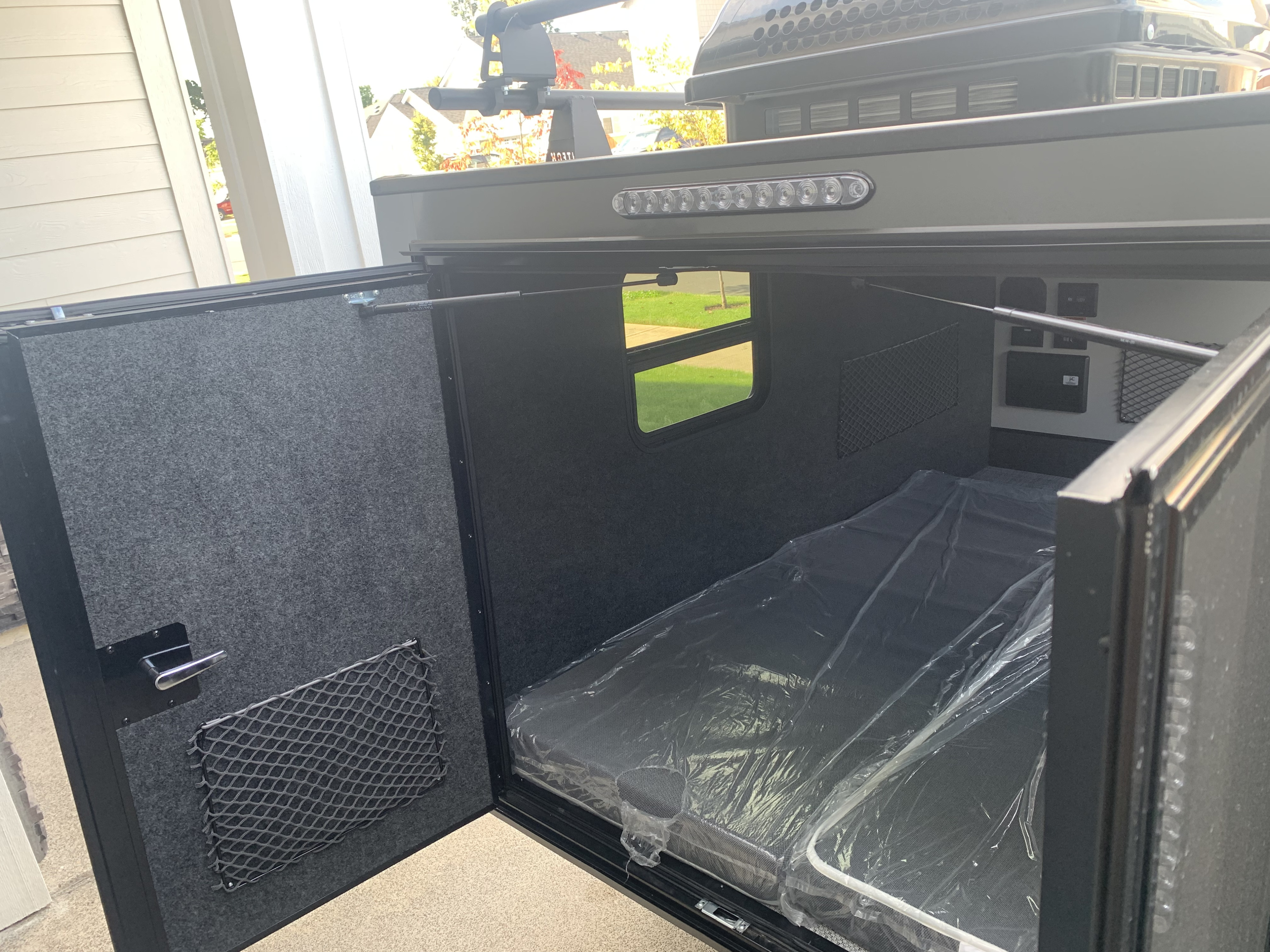 Compact RV rental camper interior, featuring a new, plastic-covered bed, carpeted walls, window, and handy storage nets.. InTech RV Flyer Pursue 2021