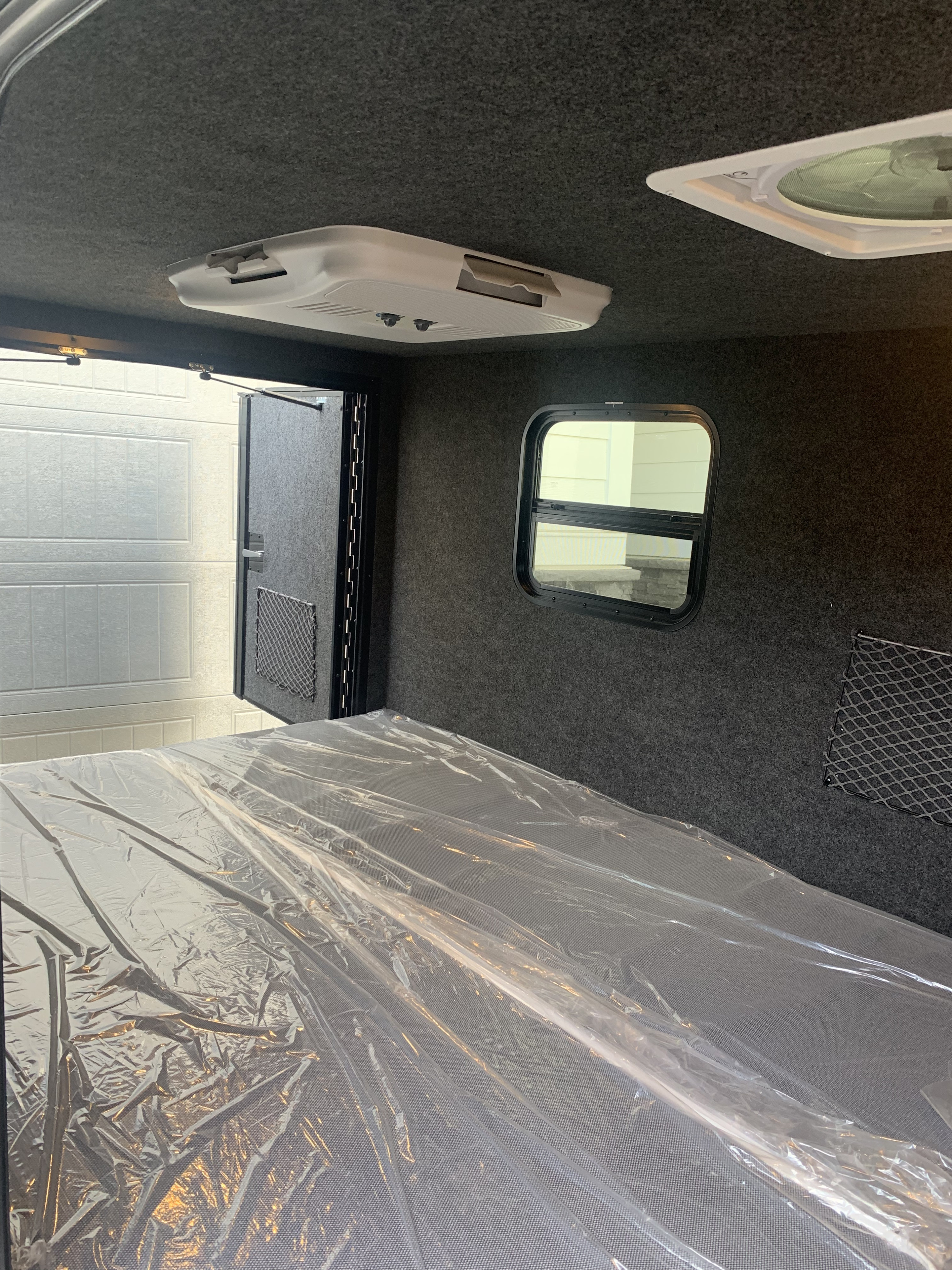 RV rental interior: new bed with protective plastic, AC unit, window, and carpeted walls. Ready for guests!. InTech RV Flyer Pursue 2021