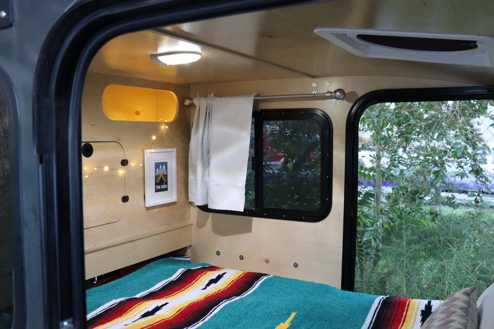 Inside a cozy RV rental: a comfortable bed with colorful blanket, window views, and warm lighting, perfect for travel.. Hiker Highway 2021