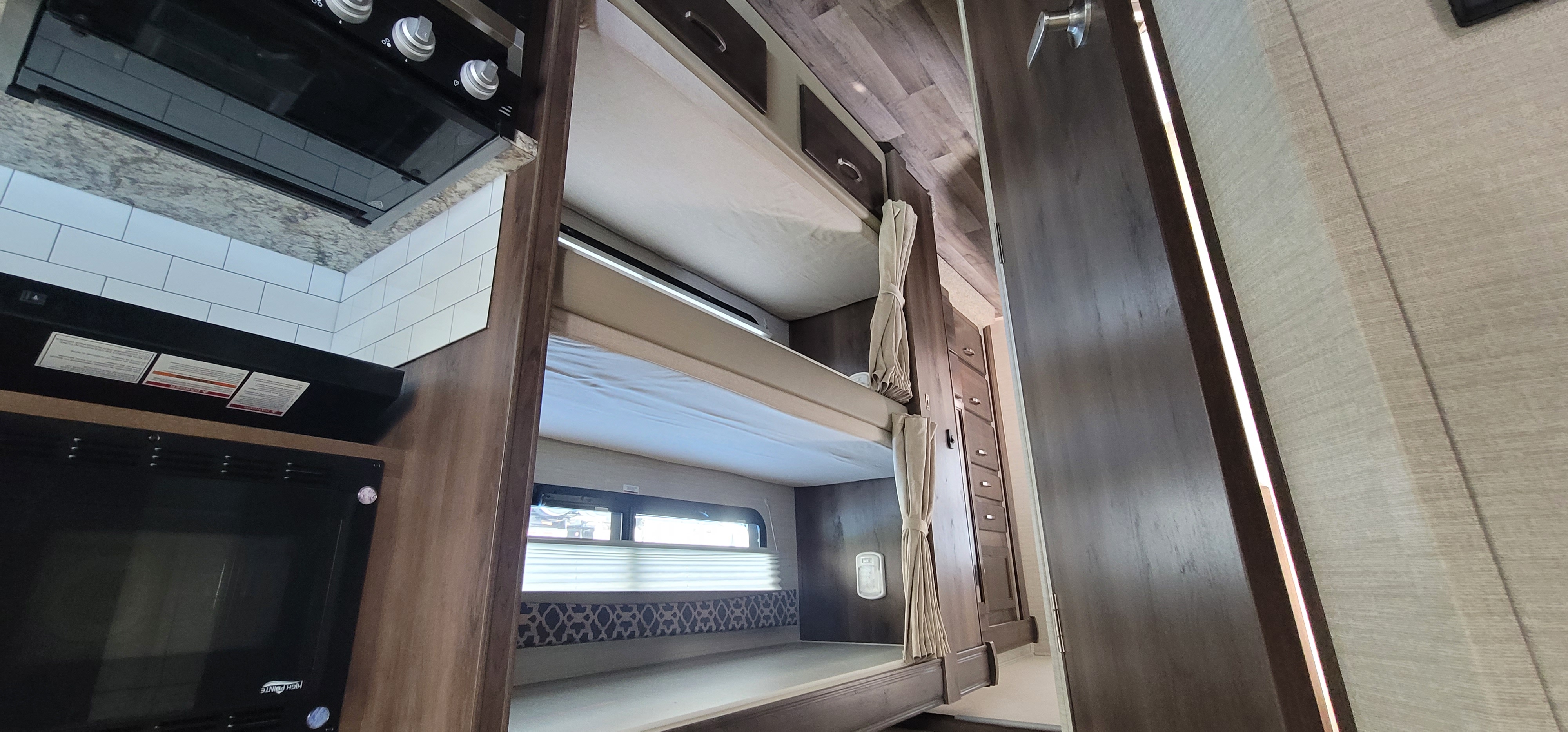 Discover this RV rental's interior: a compact kitchen with stove & microwave, plus built-in bunk beds.. Jayco Redhawk 2021