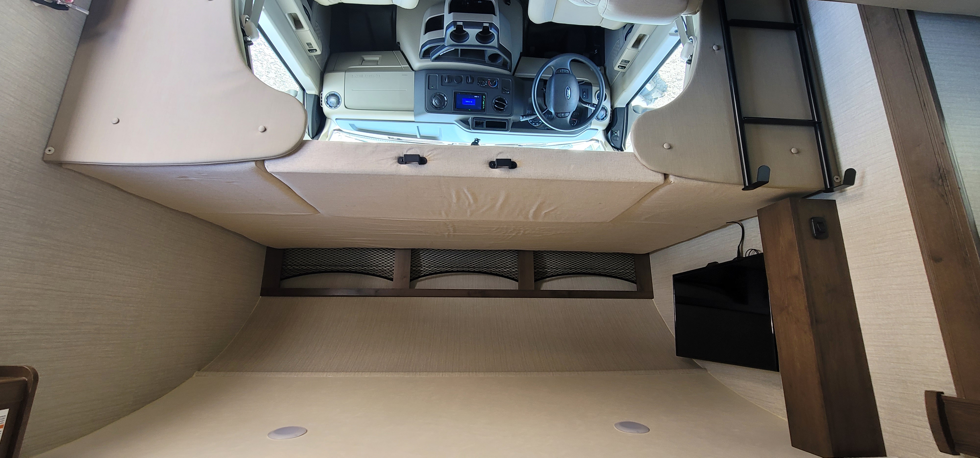 View into an RV rental cockpit from below the cab-over bunk, featuring a ladder & TV. Spacious and ready for adventure.. Jayco Redhawk 2021