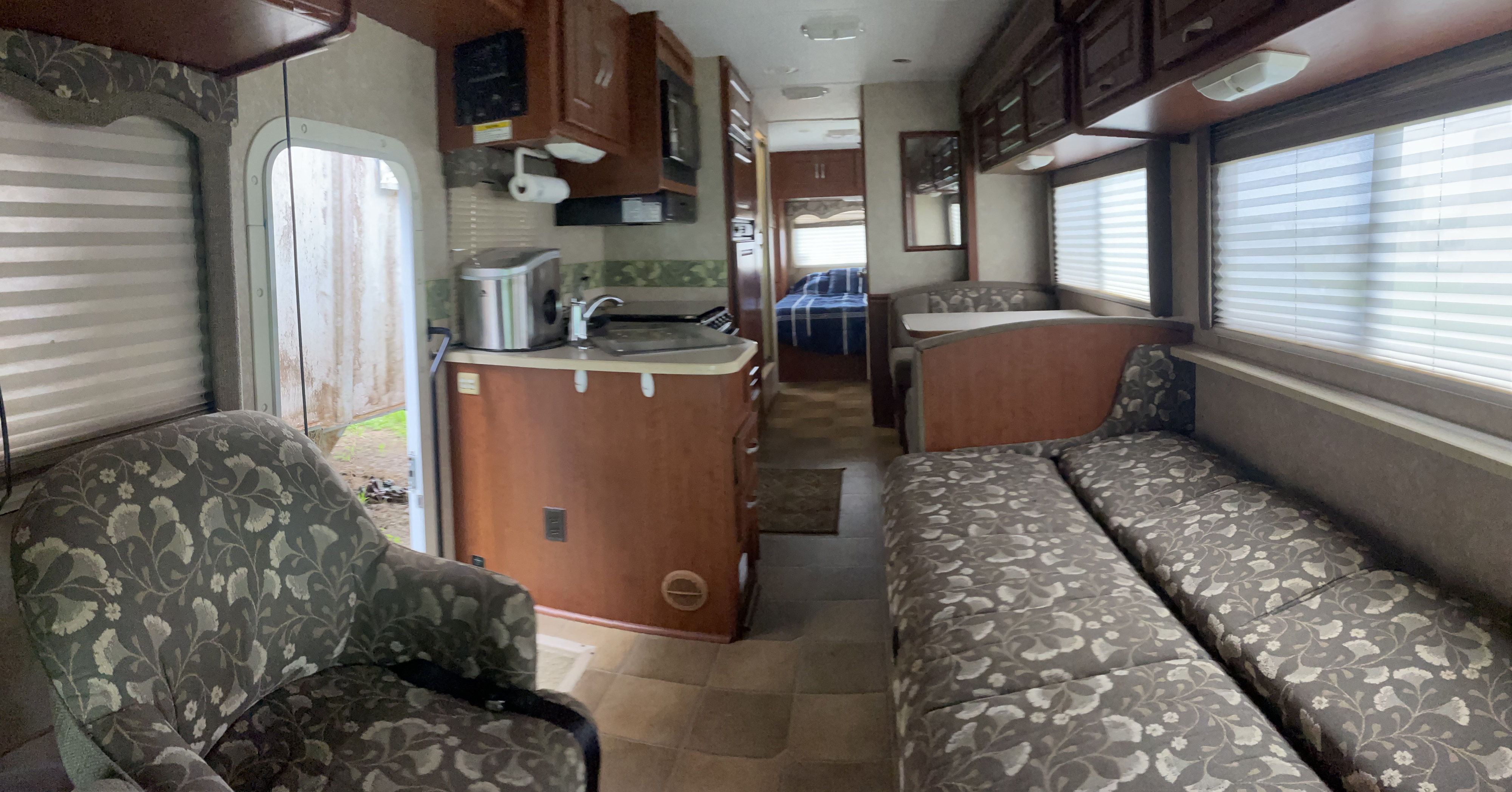 Spacious RV rental interior with a kitchen, dining booth, and floral-patterned sofa benches. Bedroom visible at the rear.. Thor Motor Coach Four Winds 2007