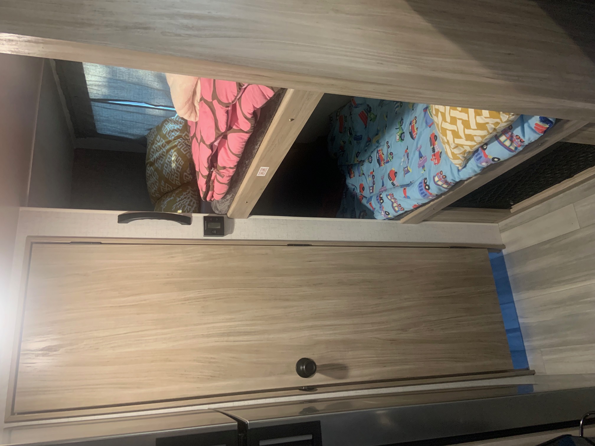 Inside an RV rental: view of a stacked bunk bed setup with vibrant bedding, light wood cabinetry, and laminate flooring.. Winnebago Micro Minnie 2021