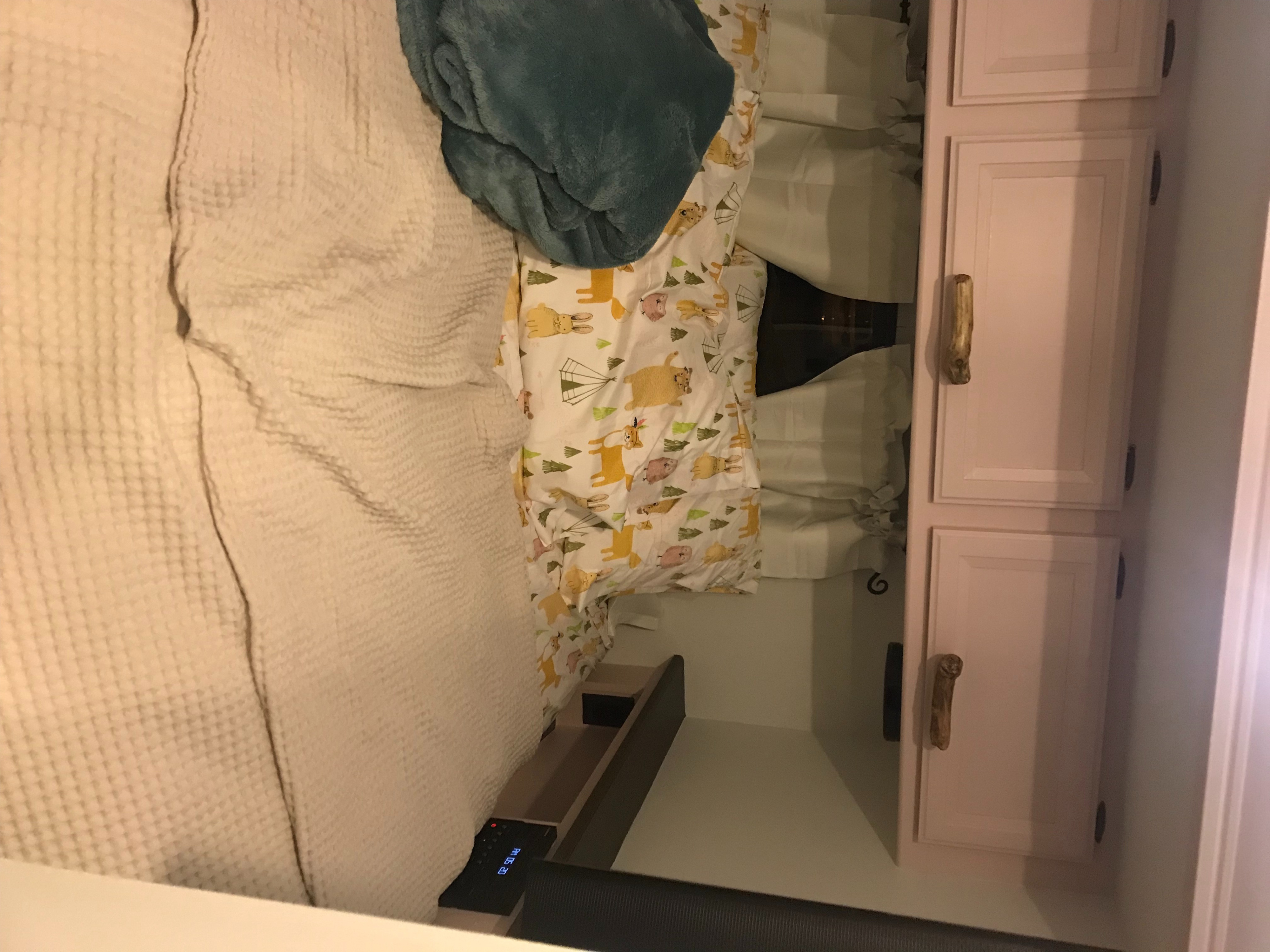 Cozy RV rental bedroom featuring light bedding, patterned sheets, a blue blanket, and pink cabinets with unique handles. Time displayed.. Thor Vegas 2016