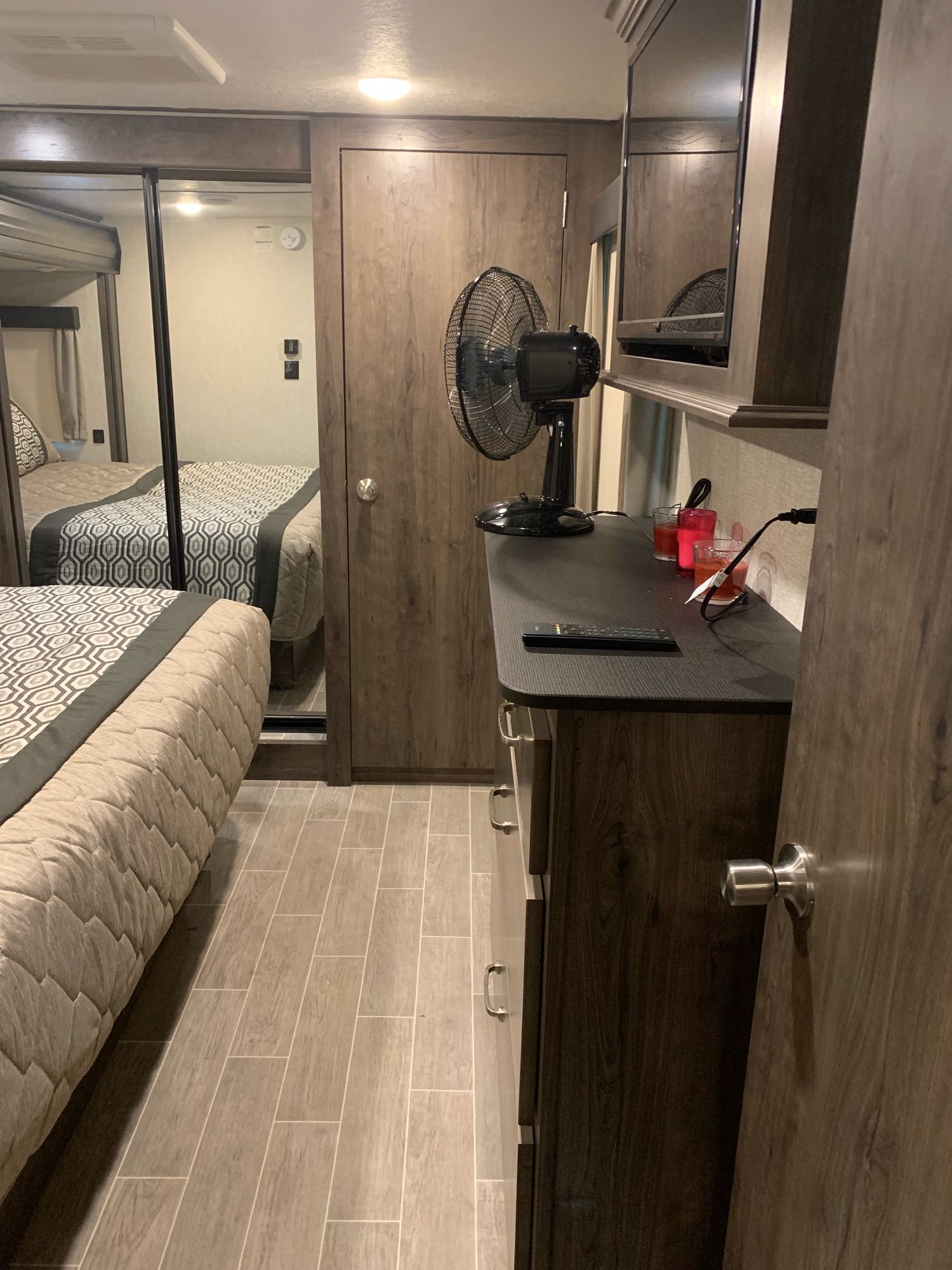 RV rental bedroom with a comfortable bed, mirrored closet, and a dresser featuring a TV and fan. Wood-look tiled floor.. Keystone Montana High Country 2019