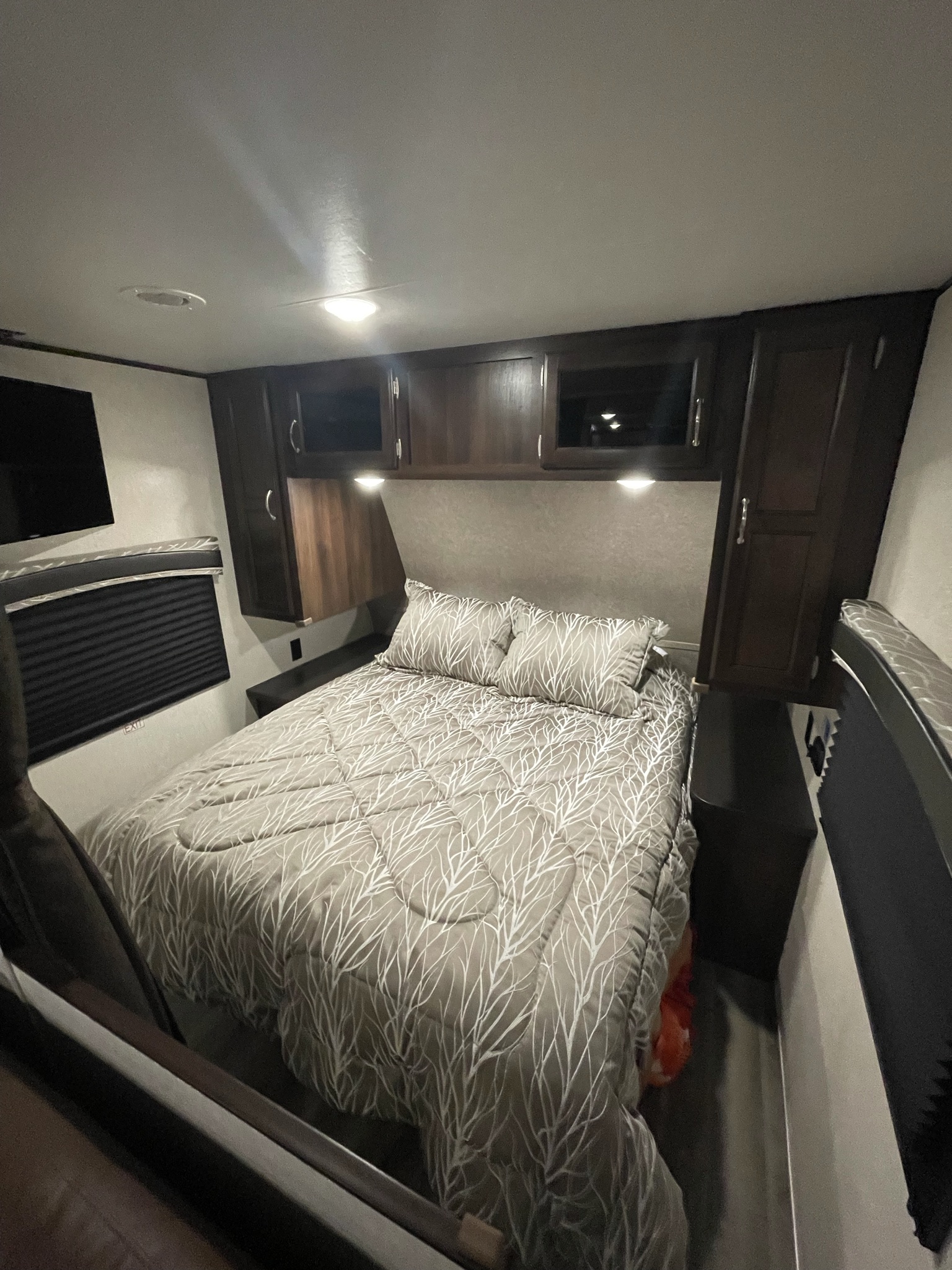 Cozy RV rental bedroom with patterned bed, overhead cabinets, and TV. Perfect for compact travel comfort.. Jayco Other 2018