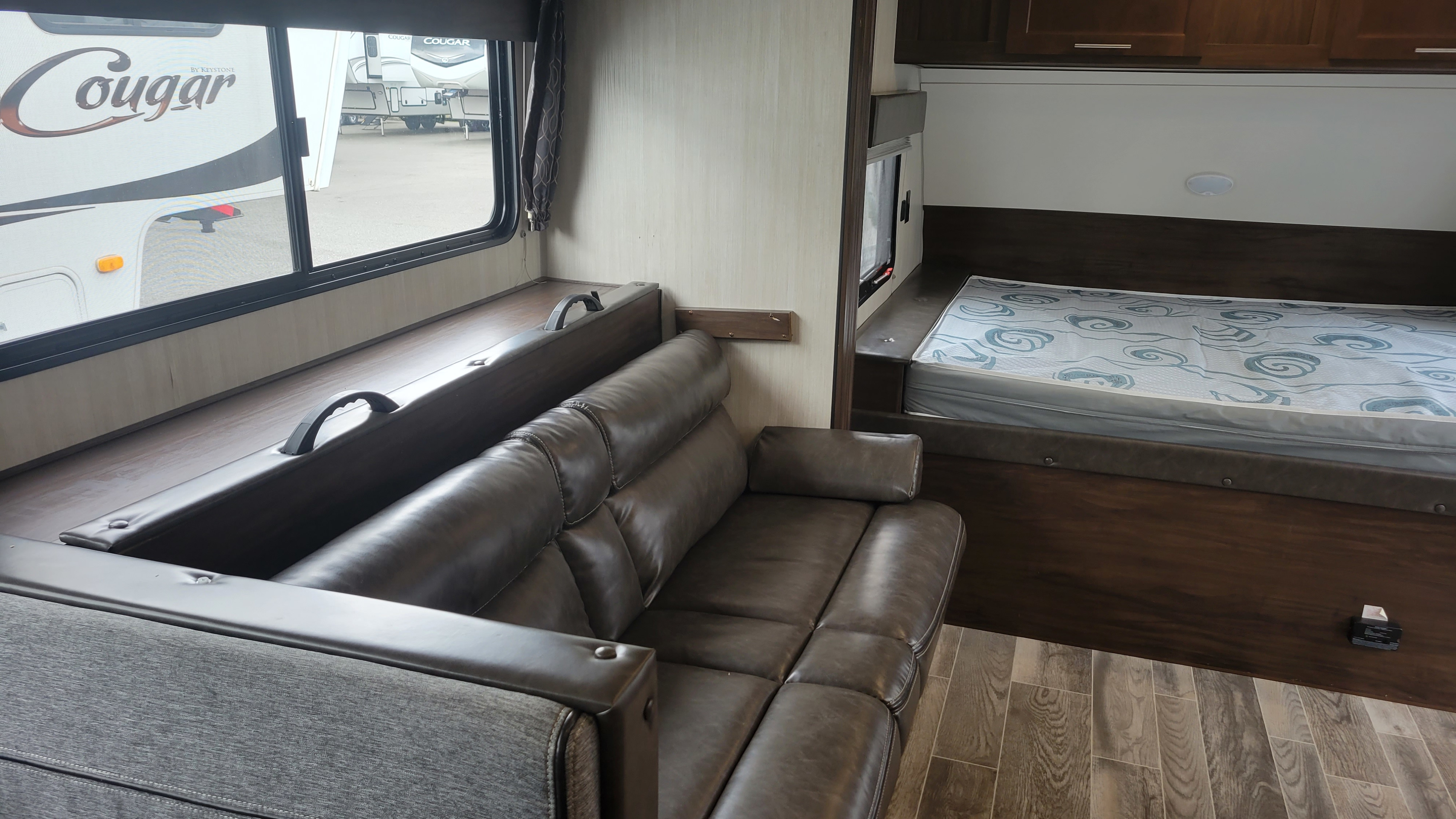 RV rental interior showing a sofa, a patterned bed in the compact bedroom, and a window overlooking other RVs.. Forest River Wolf Pup 2020