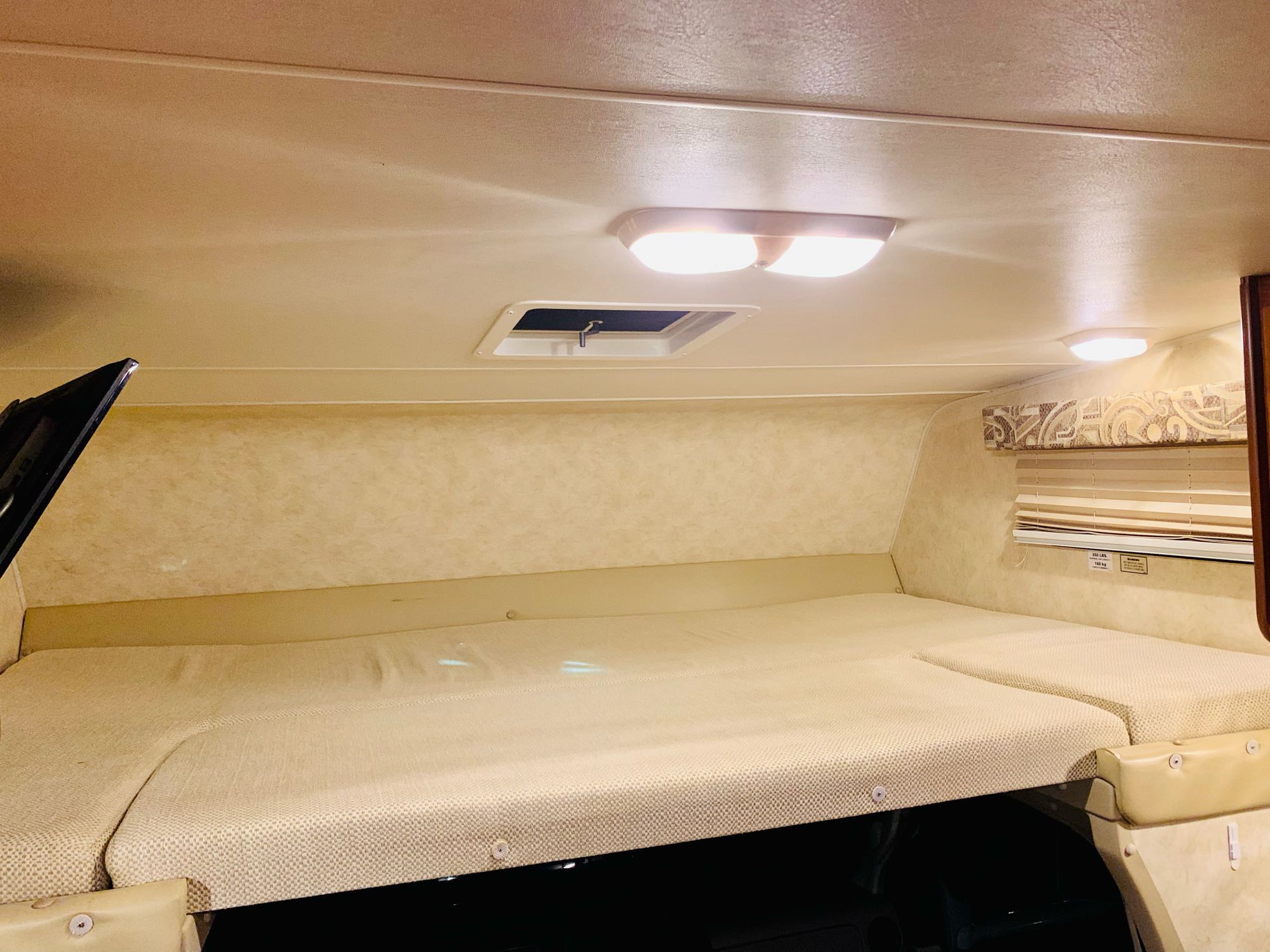 RV rental's cozy cab-over bunk bed with light-colored cushions, overhead lights, and a window. A comfortable sleeping area.. Coachman Ford E350 2013