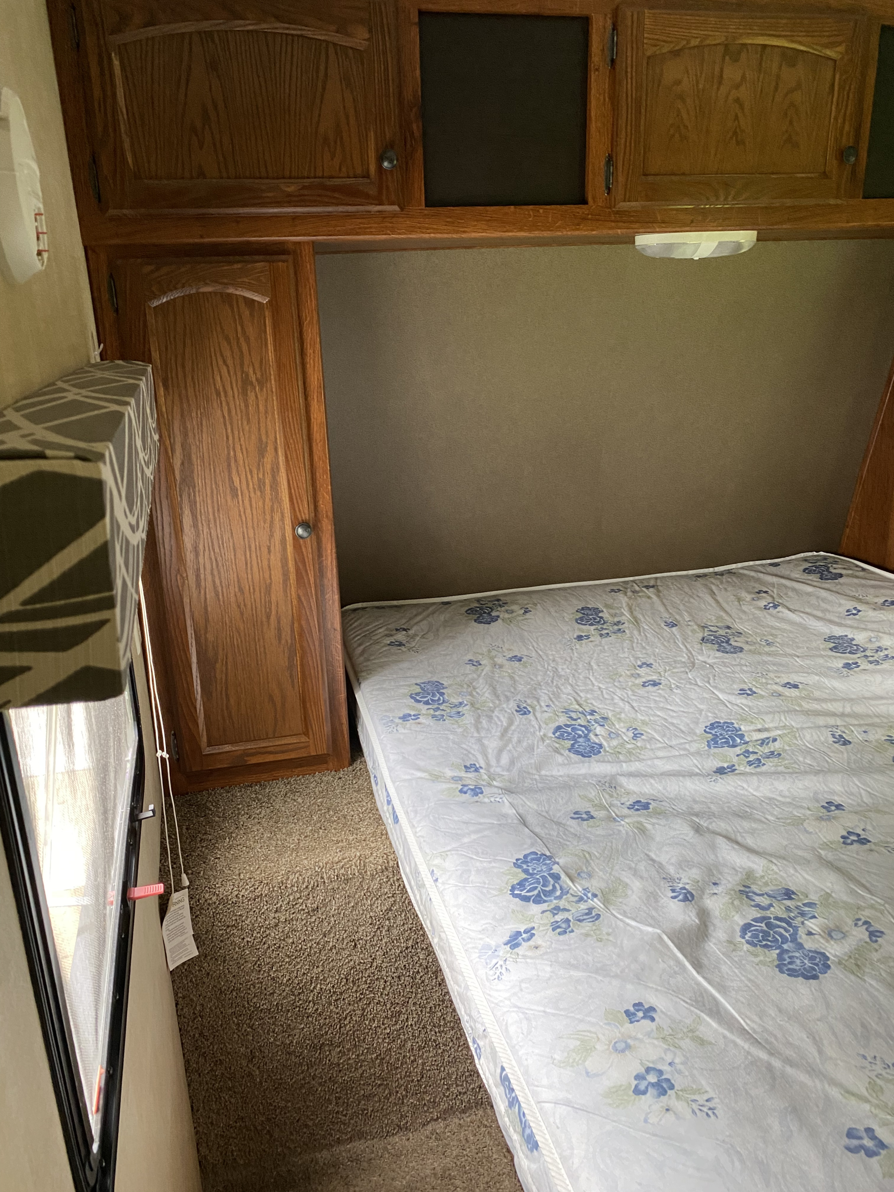 Inside an RV rental: a compact bedroom with a floral mattress, wood cabinets, and wardrobe, ideal for travel.. Keystone Hideout 2014