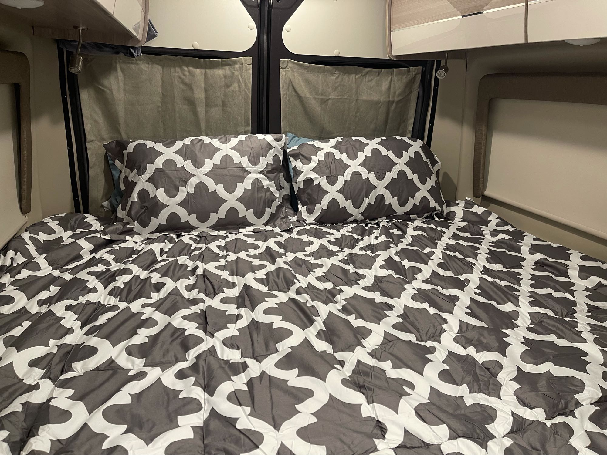 Inside an RV rental: a cozy bed with gray and white patterned comforter and pillows, ready for restful travel.. Thor Sequence 2022