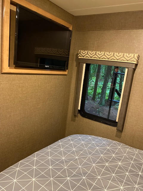 Cozy RV rental bedroom featuring a flat-screen TV, comfy bed, and a window with a scenic nature view.. Other Other 2019