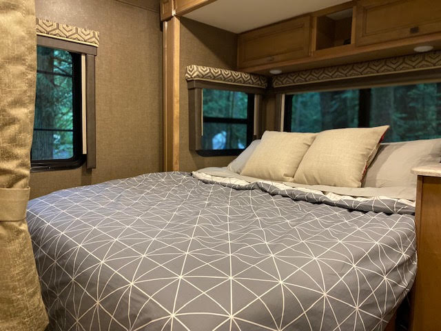 Step inside this cozy rv rental bedroom, offering a comfy bed with geometric bedding and peaceful forest views, ideal for camping.. Other Other 2019