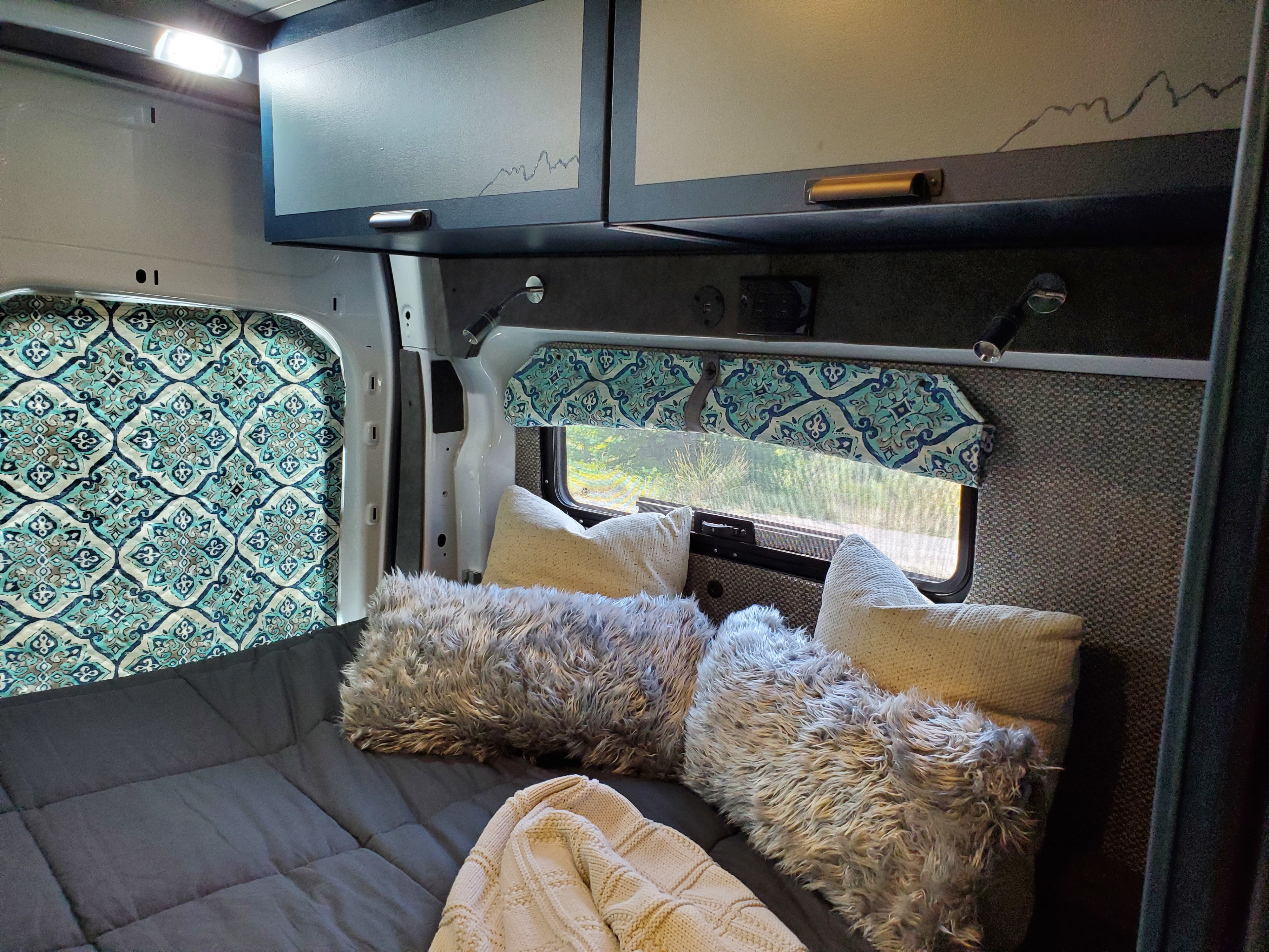 Inviting rv rental camper van bedroom with patterned accents, plush pillows, smart storage, and reading lights for a comfy trip.. Ford Transit 2019