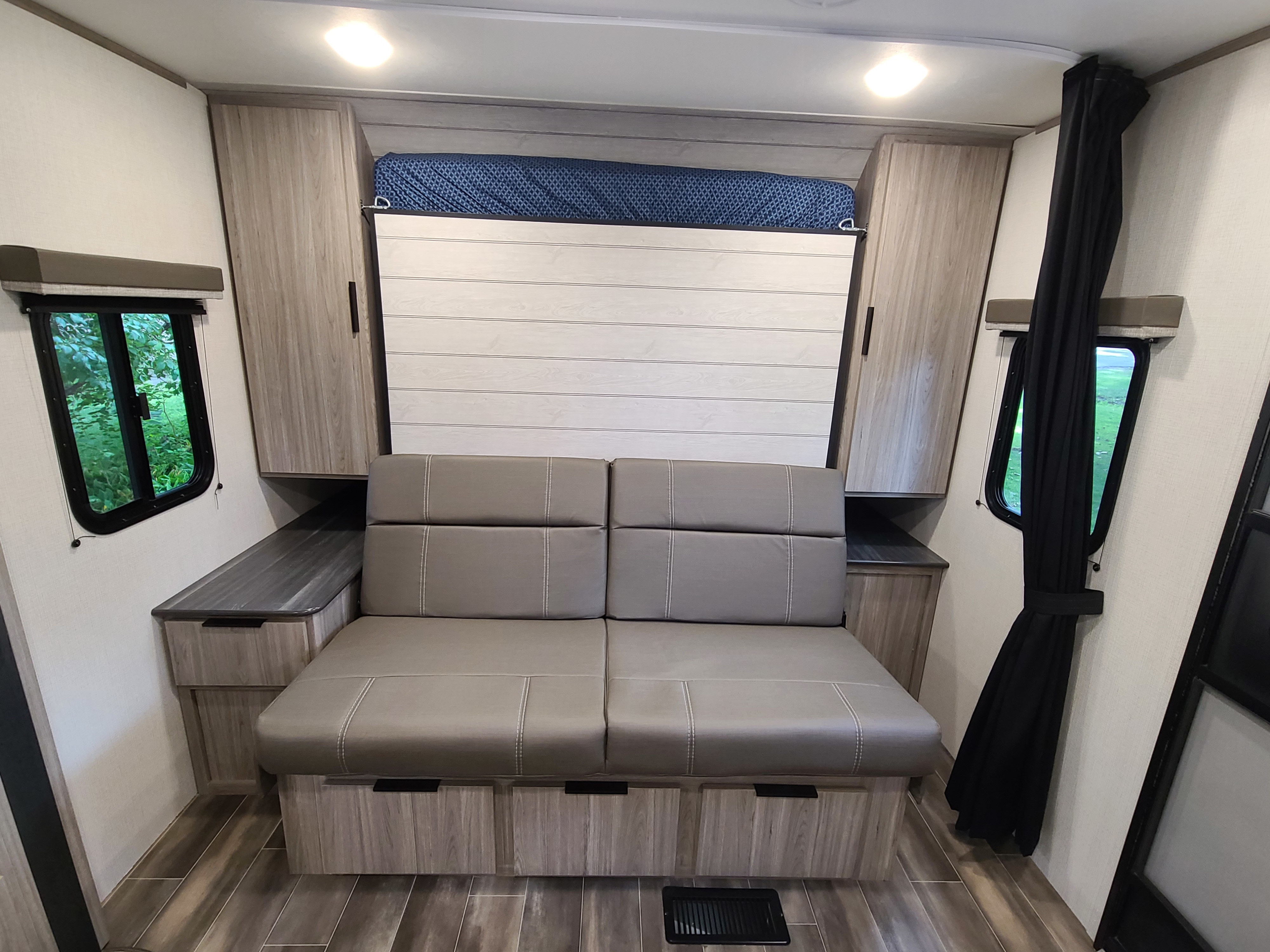 Modern RV rental interior with a gray sofa, hidden wall bed, and wood-look storage, ideal for road trips.. Keystone Passport 2021