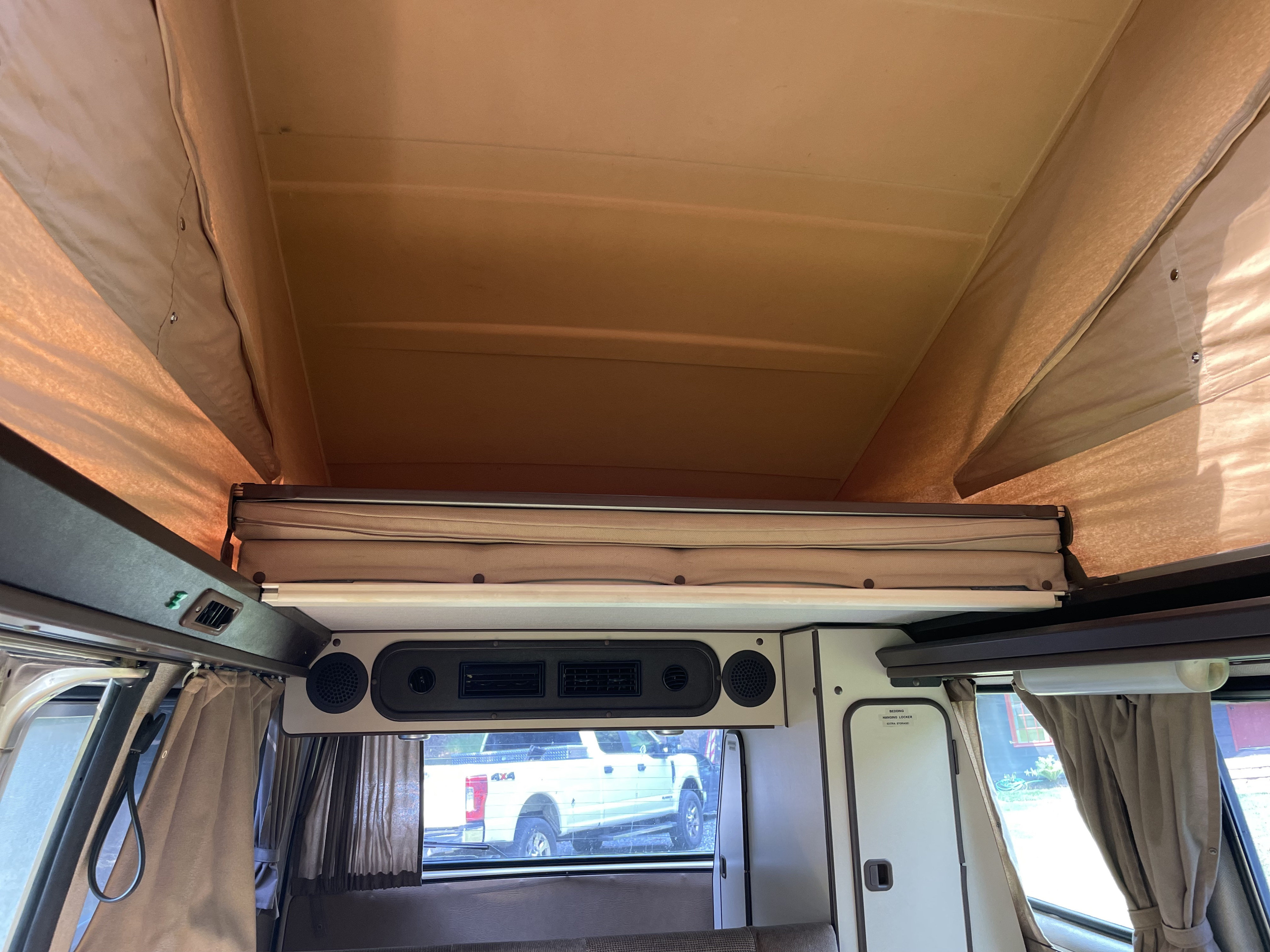 Inside a pop-top RV rental: an extended canvas roof, upper sleeping platform, and lower cabin with vents and storage.. Westfalia T3 Westfalia 1986