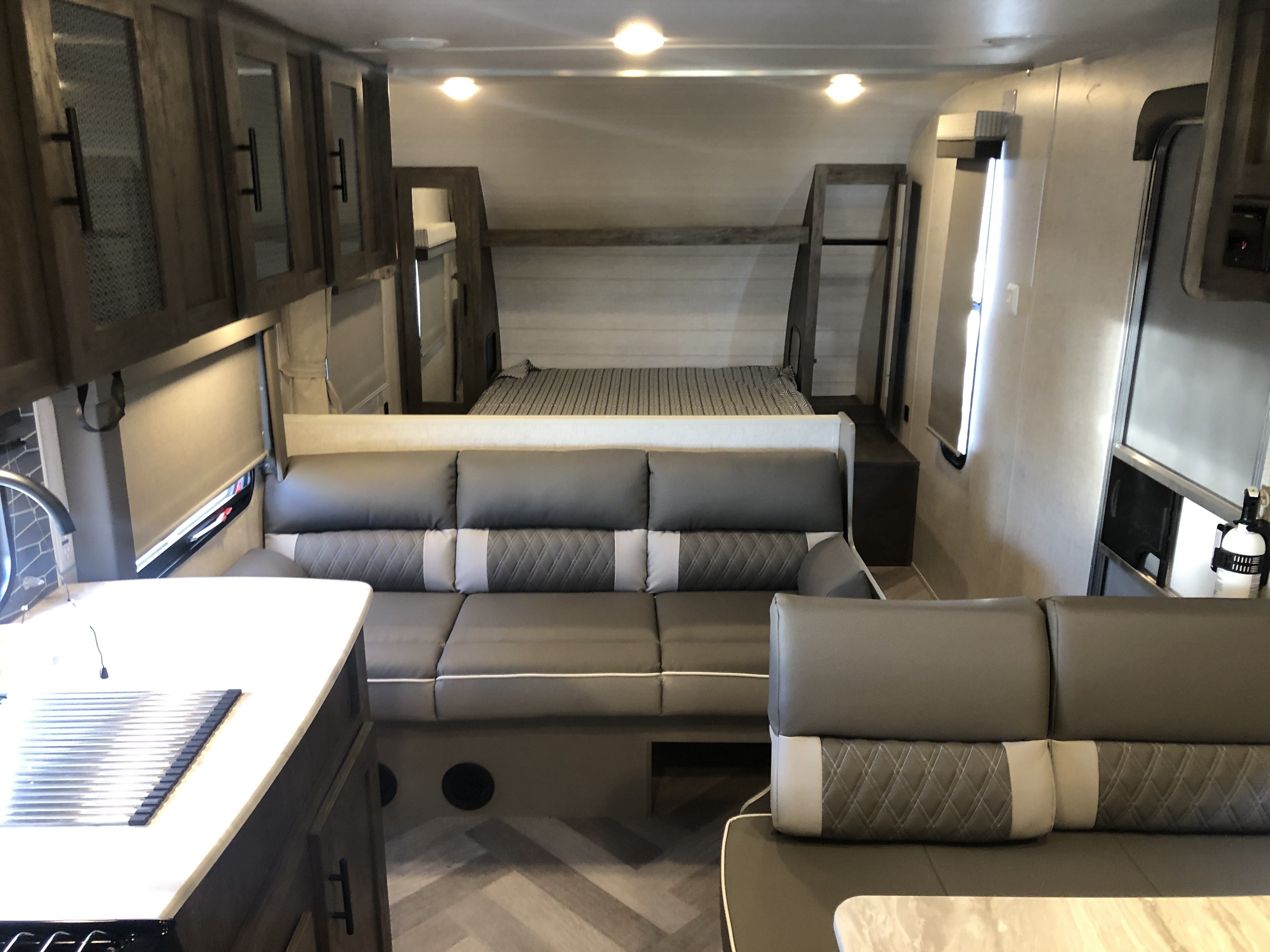 Interior view of an RV rental: includes gray dinette seating, a kitchen counter, and rear bunk beds with striped bedding.. Forest River Salem Cruise Lite 2021