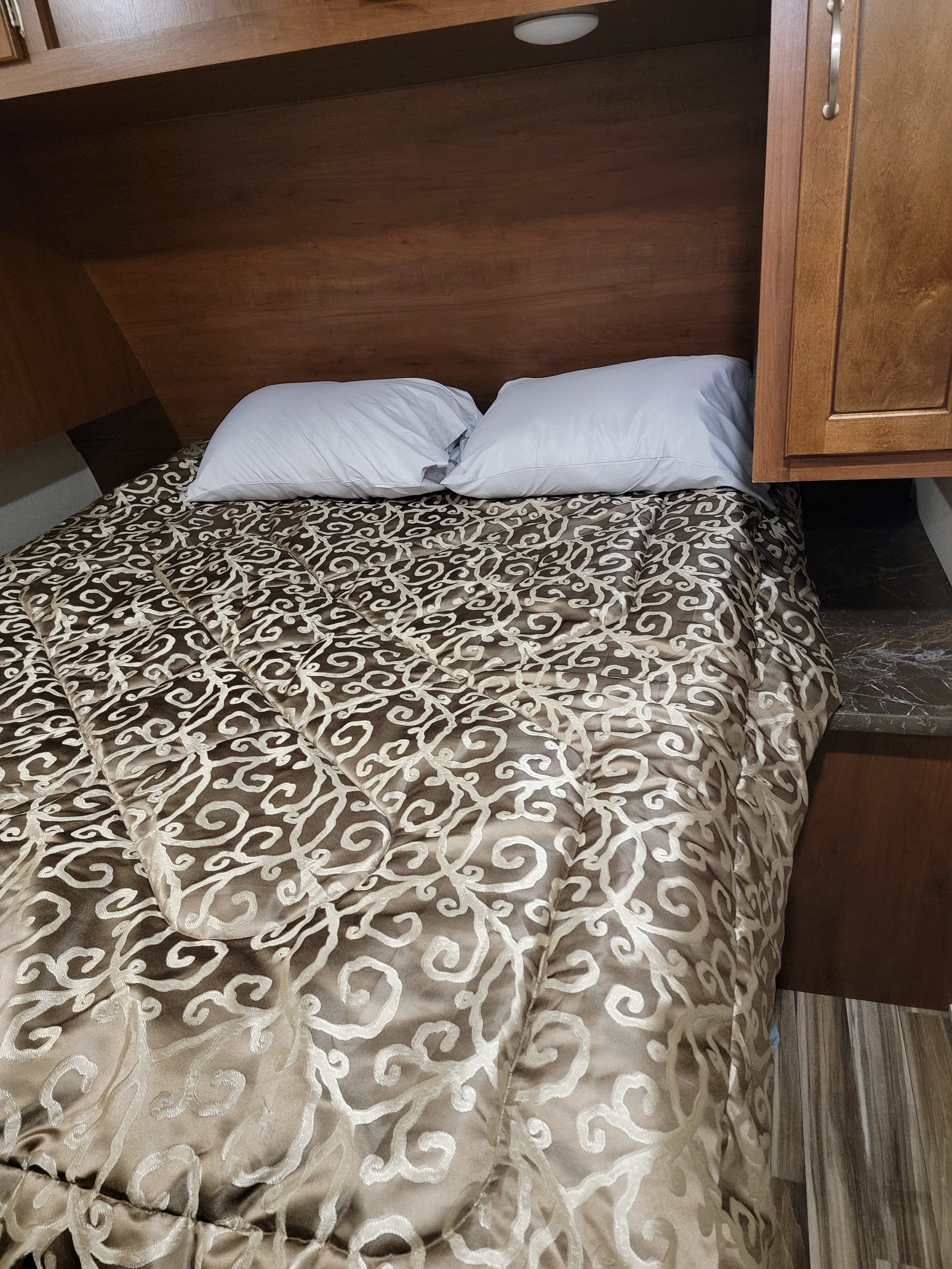 Cozy RV rental bedroom with patterned comforter and white pillows, featuring wood cabinetry and a small light.. Jayco Jay Flight 2017