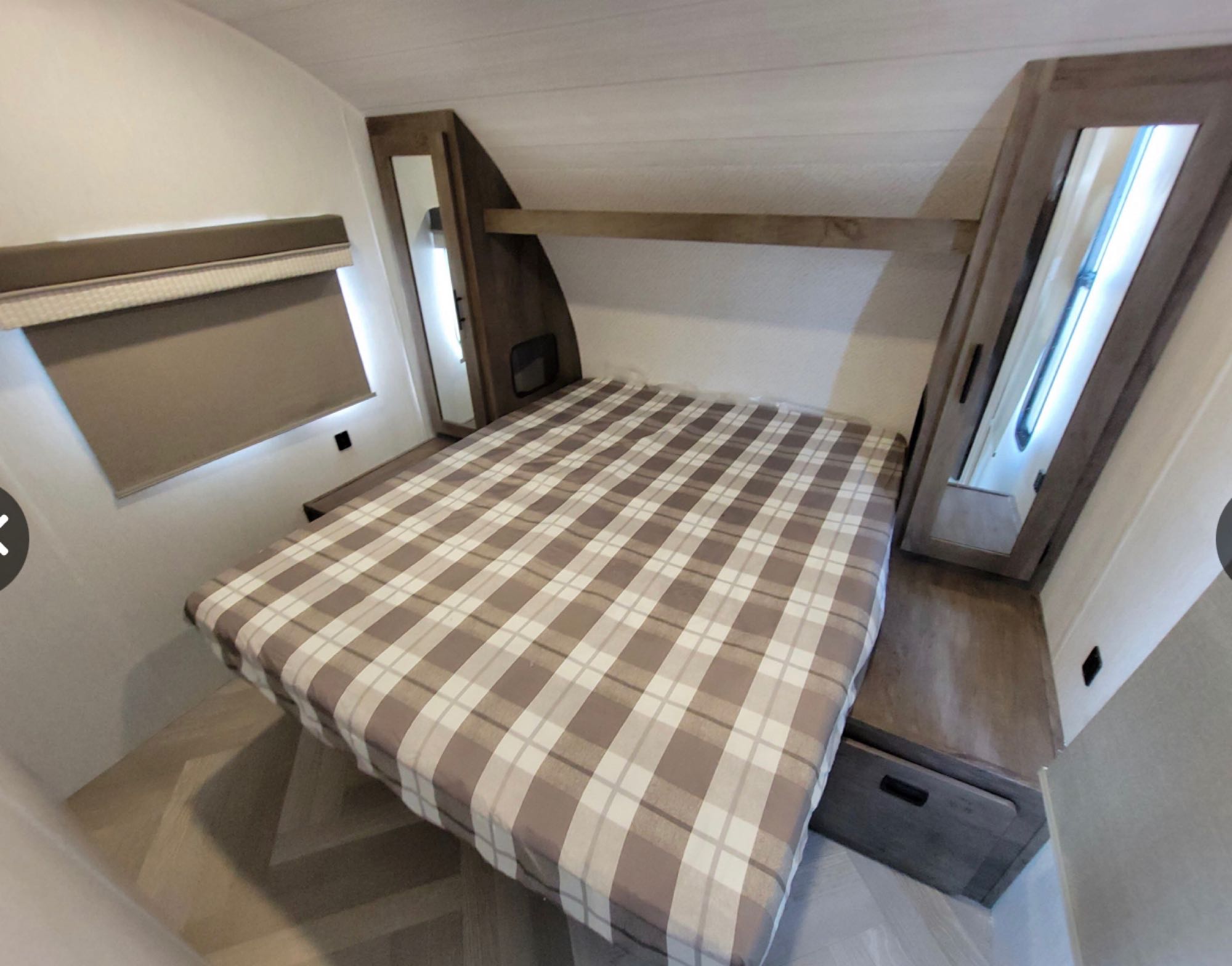 RV rental's inviting bedroom: plaid bed, built-in storage, and window blinds for a cozy stay.. Forest River Wildwood X-Lite 2022