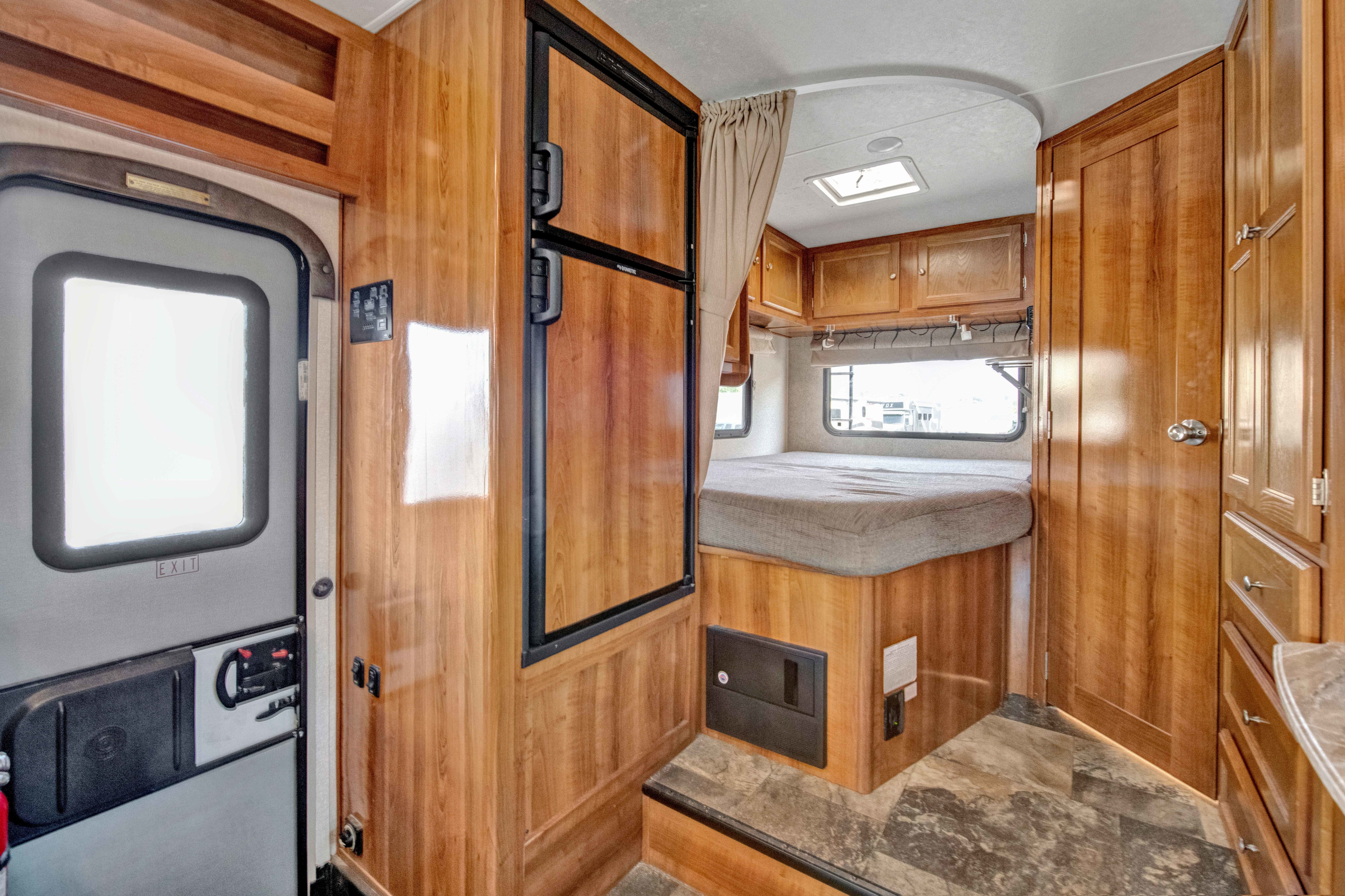 RV rental interior: a cozy living space with a bed, refrigerator, and exit door, ideal for your road trip adventures.. Forest River Coachmen Leprechaun 2019