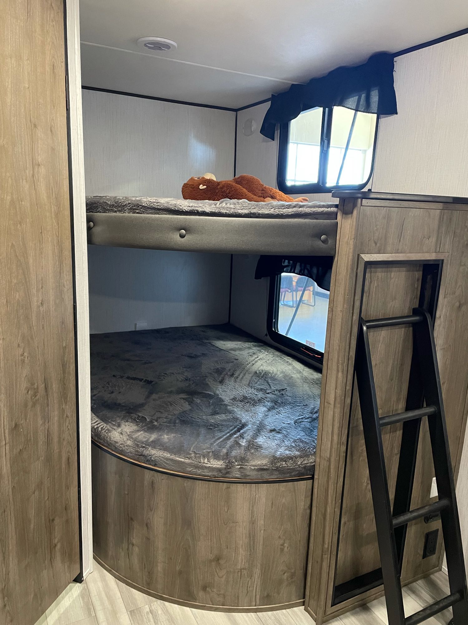 RV rental interior features bunk beds with grey mattresses, a plush toy, and ladder for access. Windows visible.. Pioneer 27fqs 2021