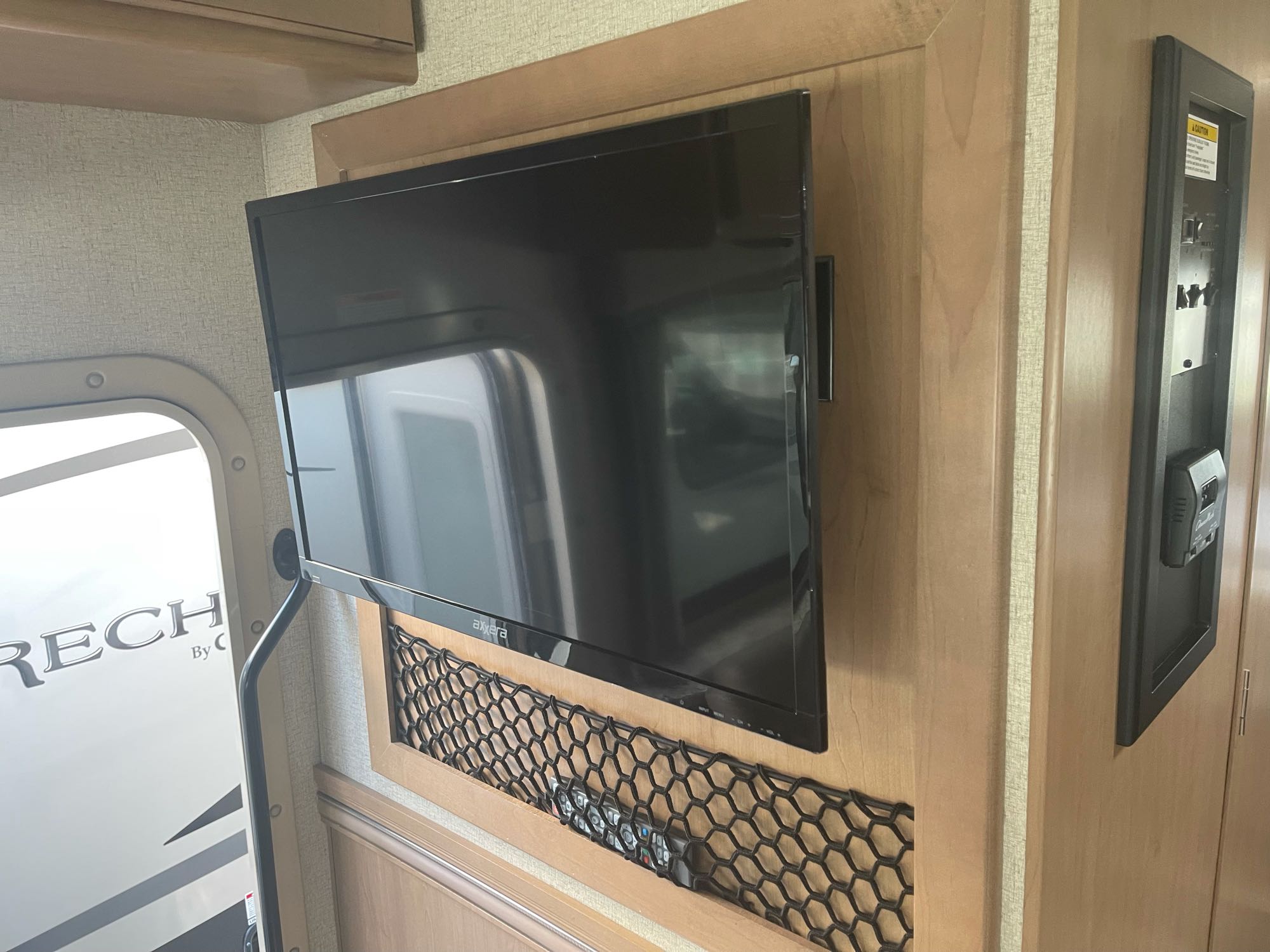 Inside an RV rental: mounted TV, honeycomb storage net with remotes, and a control panel on a wood wall.. Thor Motor Coach Four Winds 2021