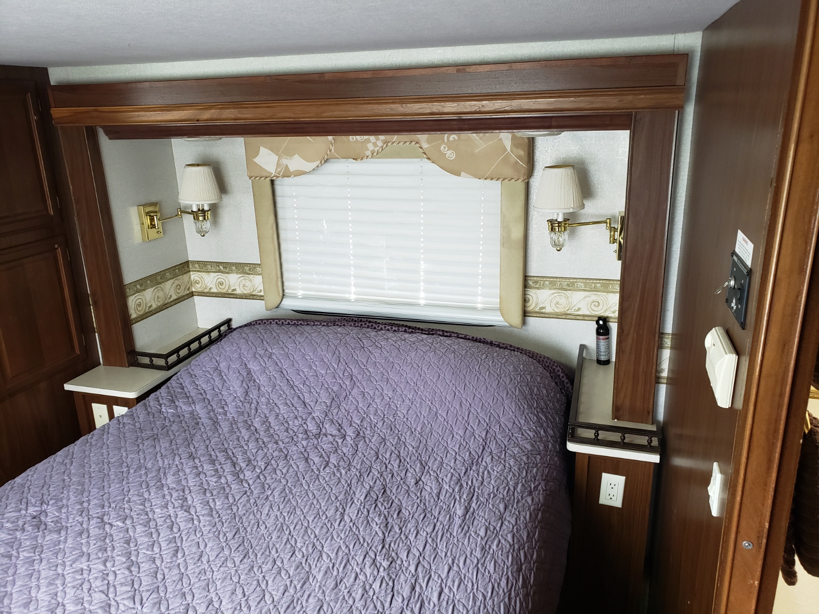 Comfortable RV rental bedroom featuring a purple bed, window, and integrated side tables. Perfect for a camper's retreat.. Fleetwood Revolution 2002