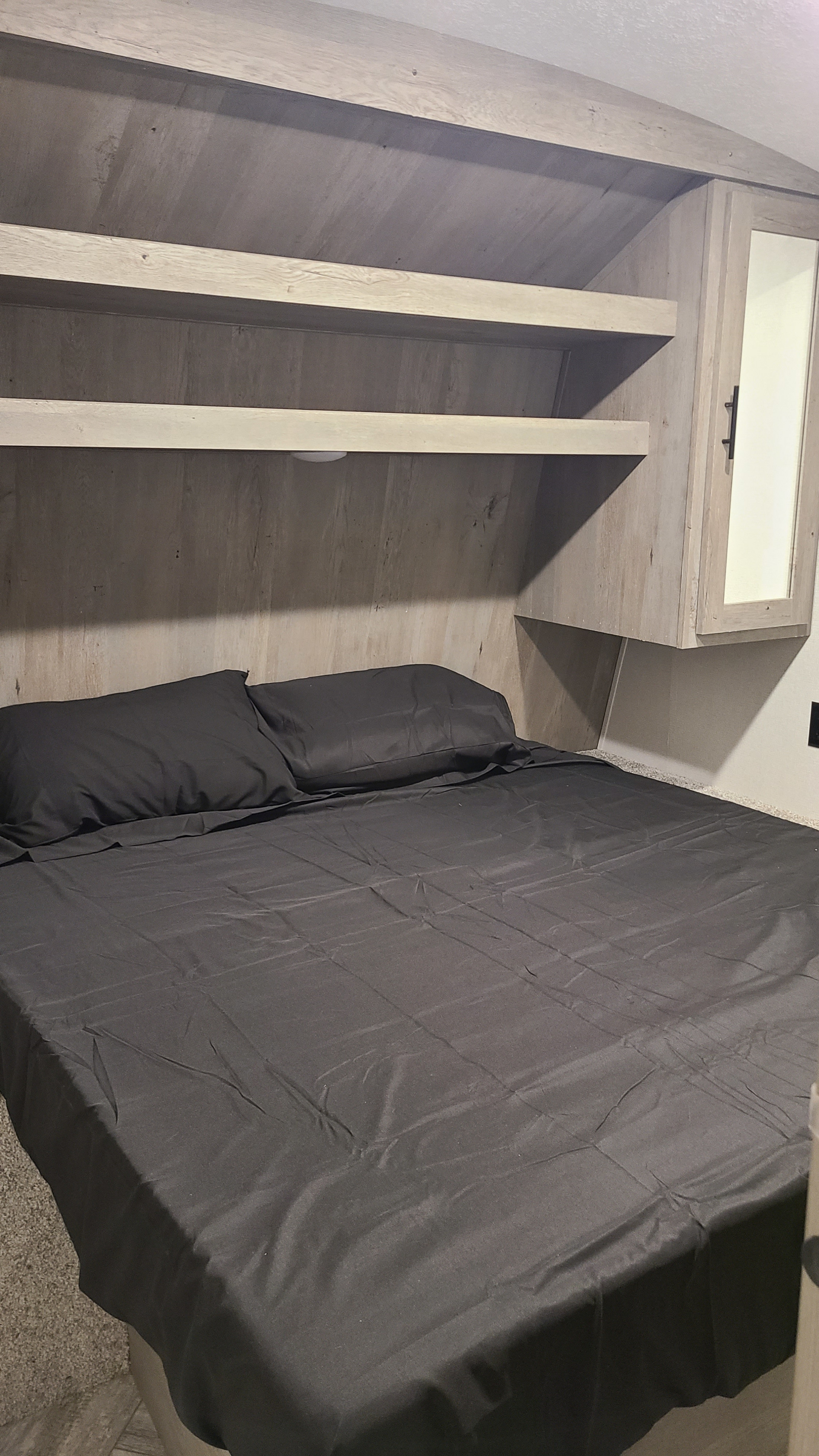 Cozy RV rental bedroom featuring a bed with dark sheets, built-in wooden shelves, and a mirrored cabinet.. Keystone Springdale 2022