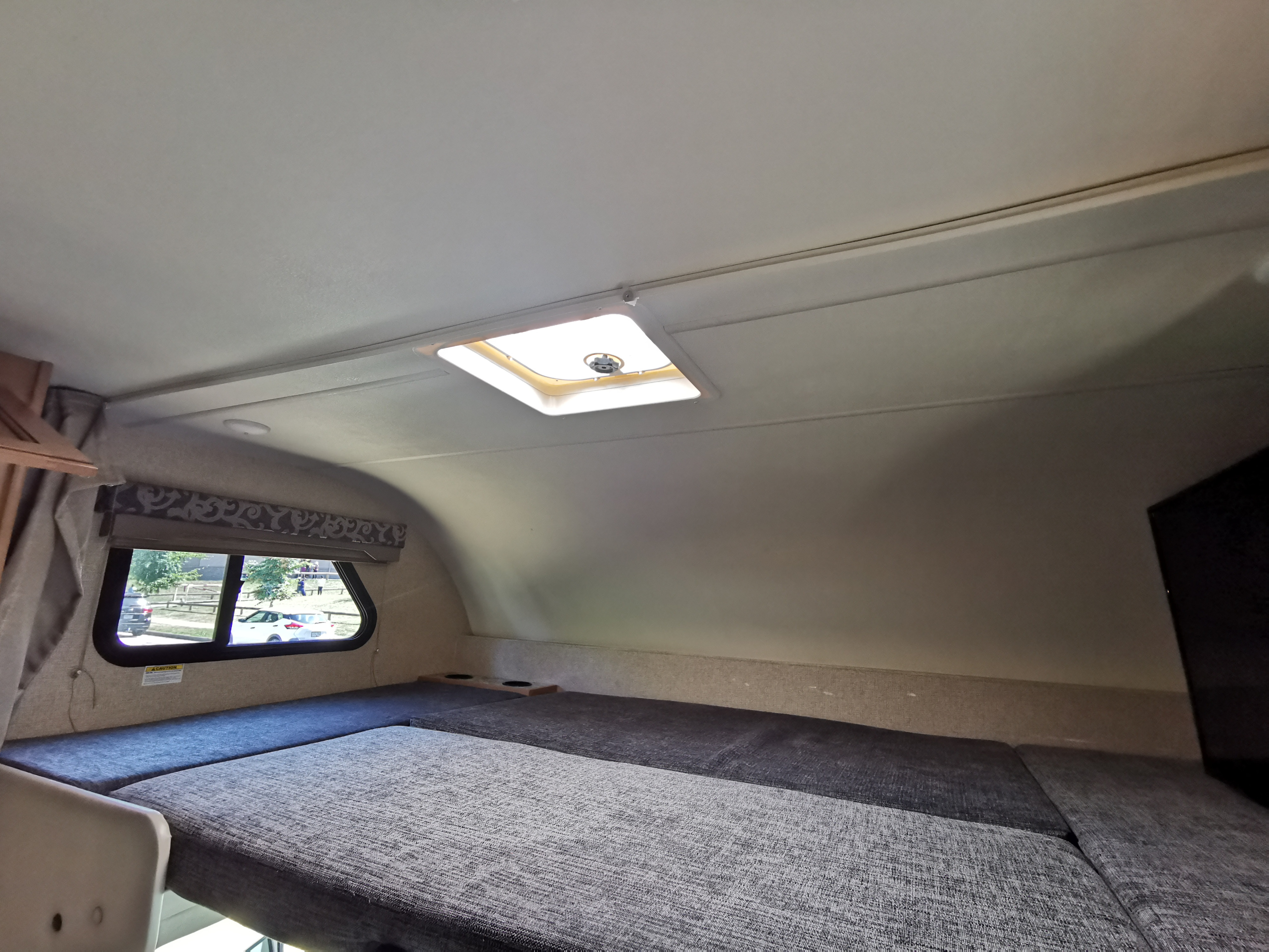 RV rental's comfortable cab-over bunk bed with grey cushions, a window, and skylight above for travelers.. Thor Four Winds 2017