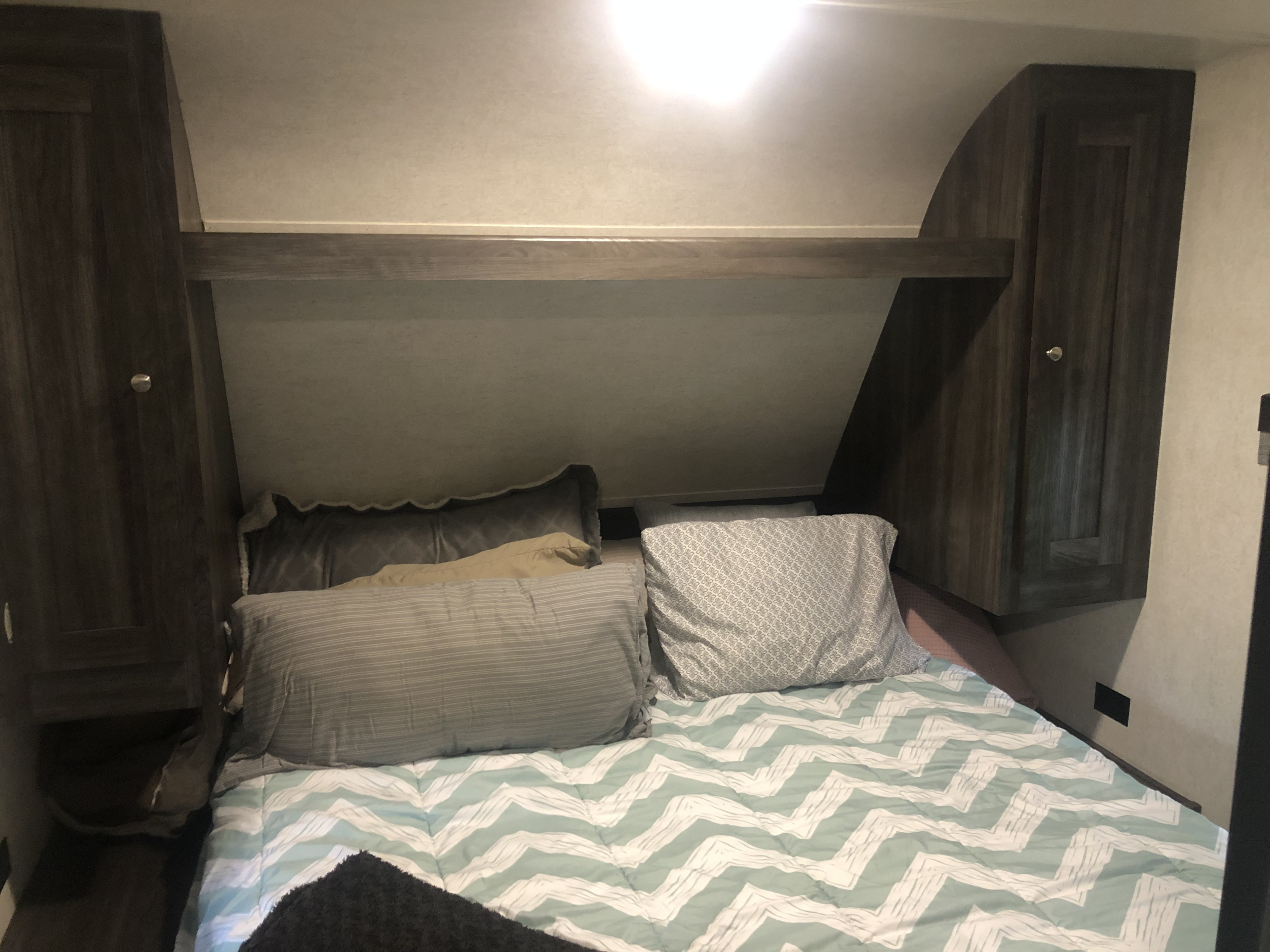 Inside an RV rental: a compact bedroom with a bed, cozy bedding, and built-in overhead cabinets.. Jayco Highland Ridge 2019
