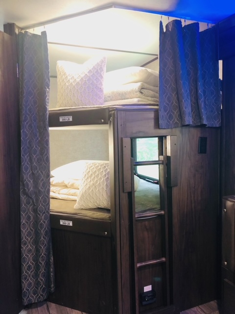 Interior view of an RV rental showing stacked bunk beds with white bedding and privacy curtains, each rated for 300 lbs.. Forest River Cherokee Alpha Wolf 2018