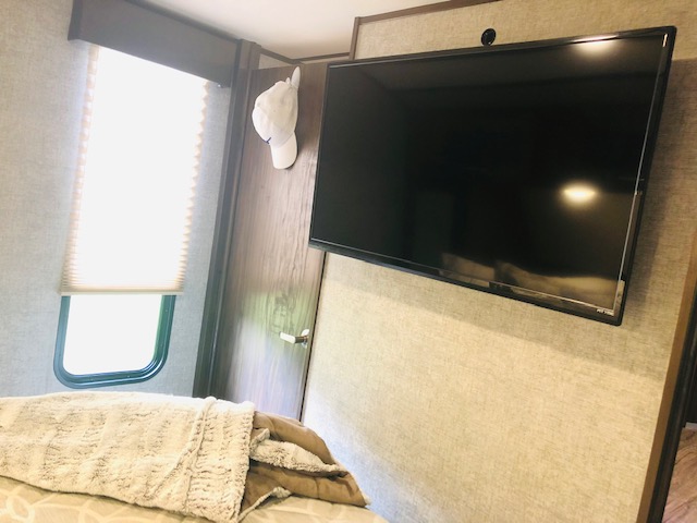 Cozy RV rental bedroom featuring a mounted TV, window with blinds, and inviting bed. Ideal for comfortable travel.. Forest River Cherokee Alpha Wolf 2018
