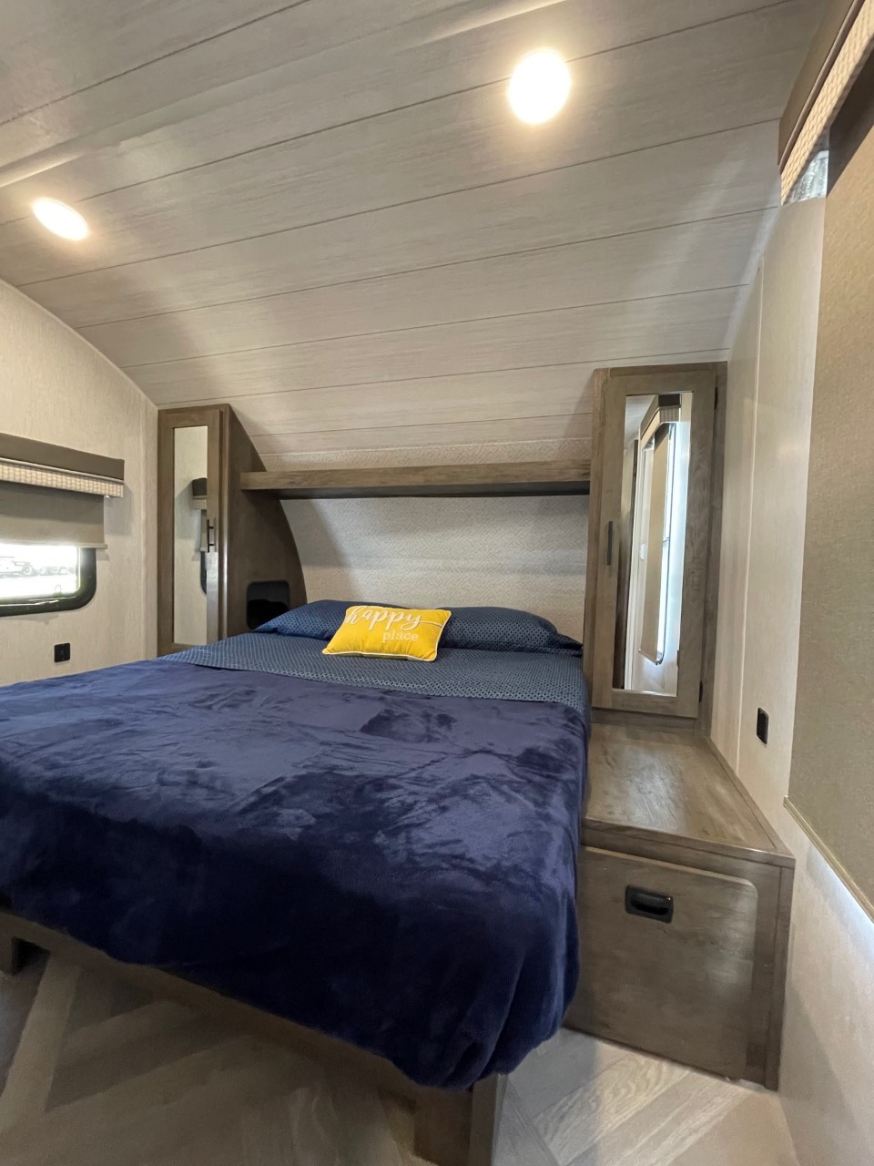 RV rental bedroom: A compact, cozy space with a dark blue bed, overhead lights, and built-in wood storage.. Forest River Salem Cruise Lite 2022