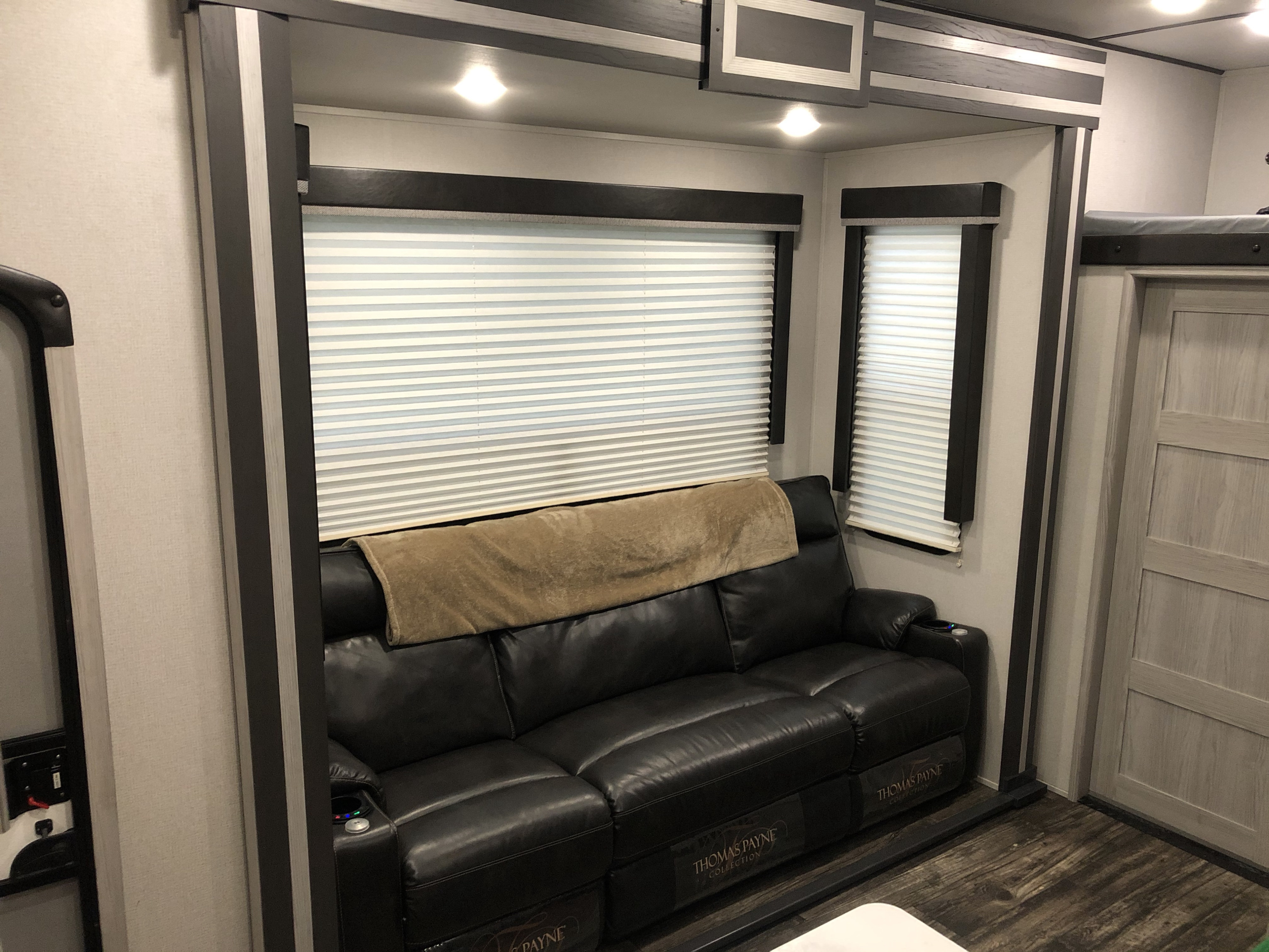 Cozy RV rental features a Thomas Payne Collection leather recliner sofa with a tan blanket, blinds, and modern trim.. Keystone Fuzion 2021