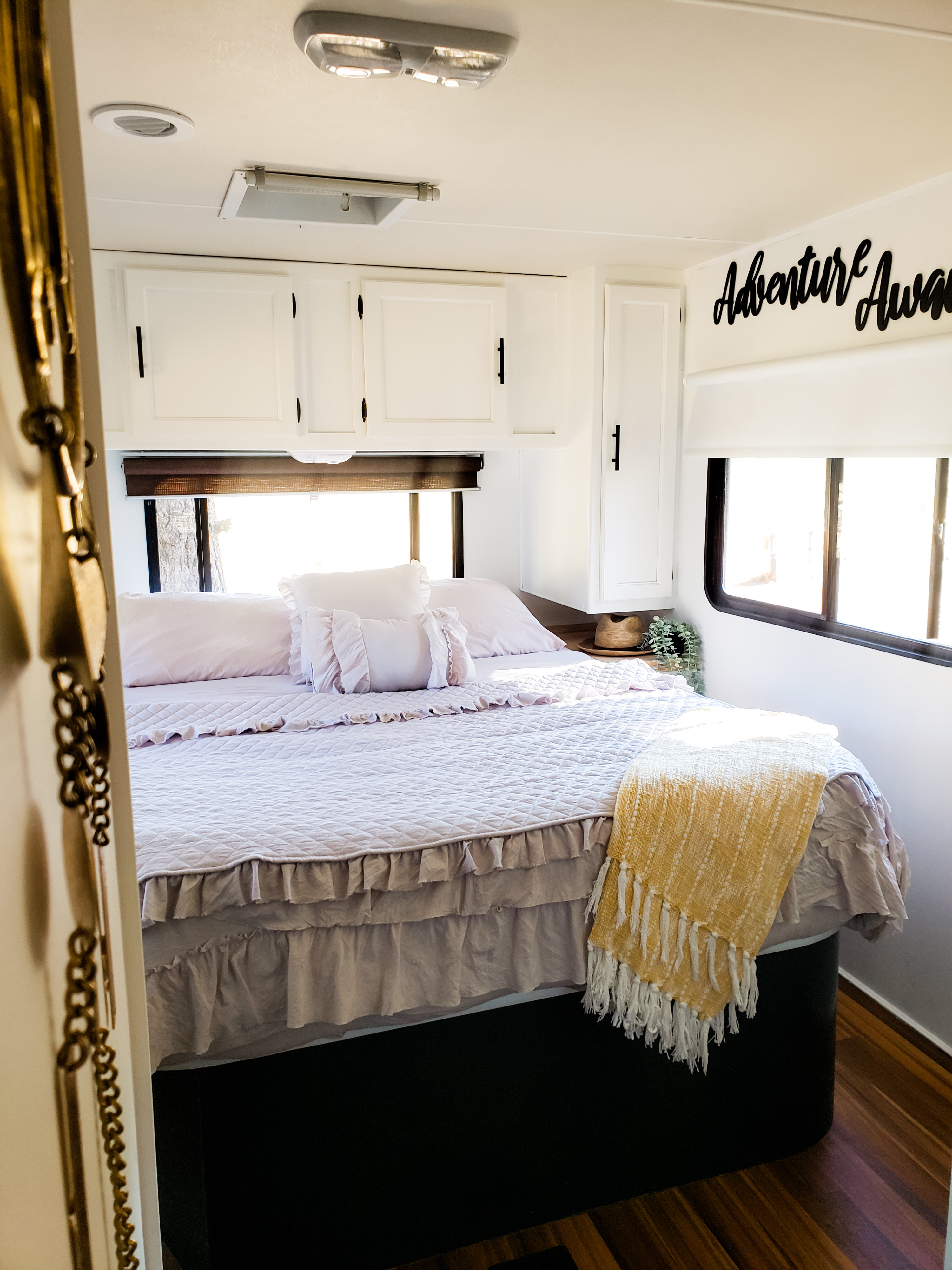 Cozy RV rental bedroom featuring soft lavender bedding, a bright yellow throw, and "Adventure Awaits" decor.. Coachmen Freelander 2014