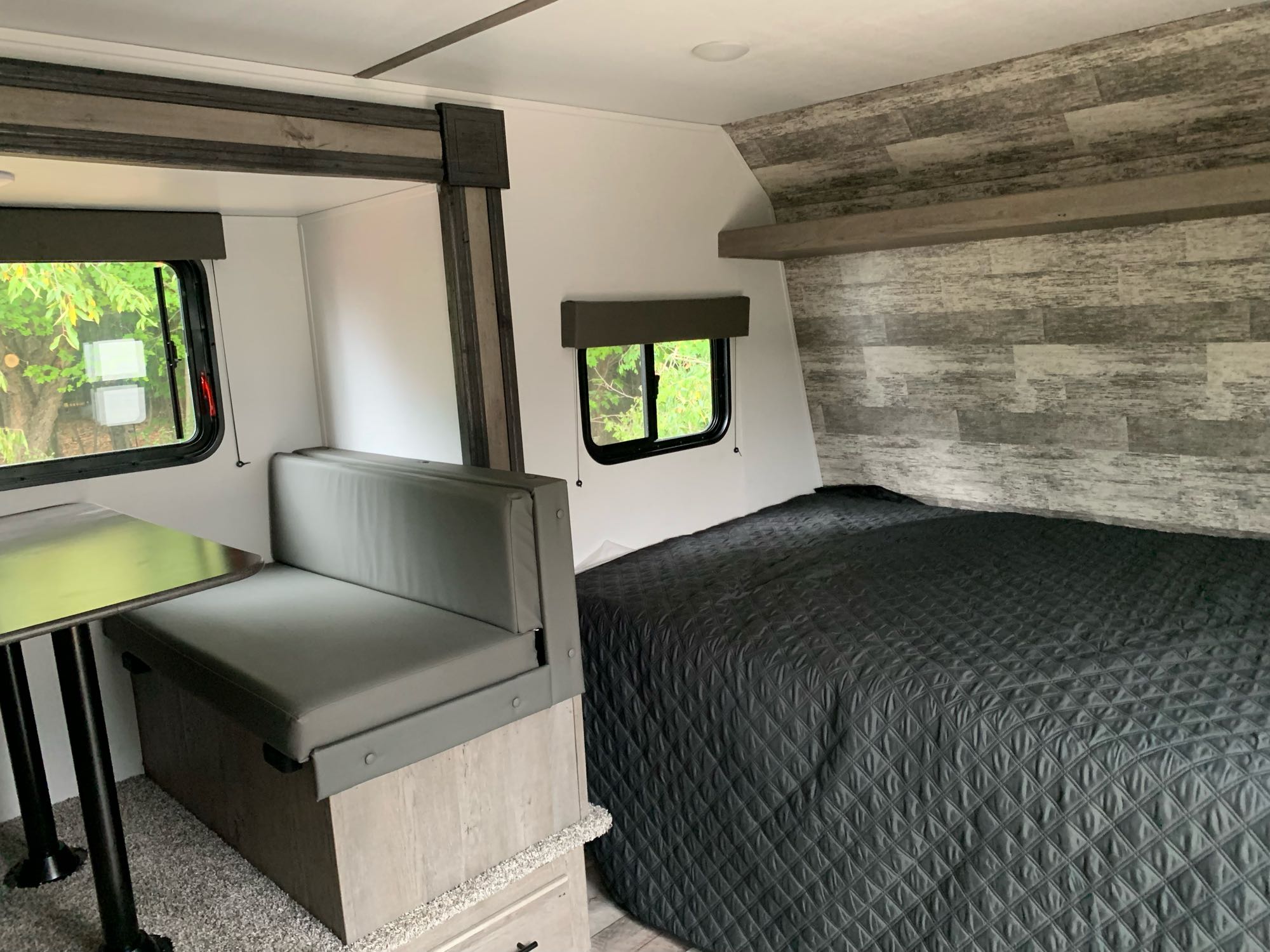 Cozy rv rental interior: a dinette with bench seating, a table, and a spacious bed with a quilted cover are visible.. Keystone Springdale 2021
