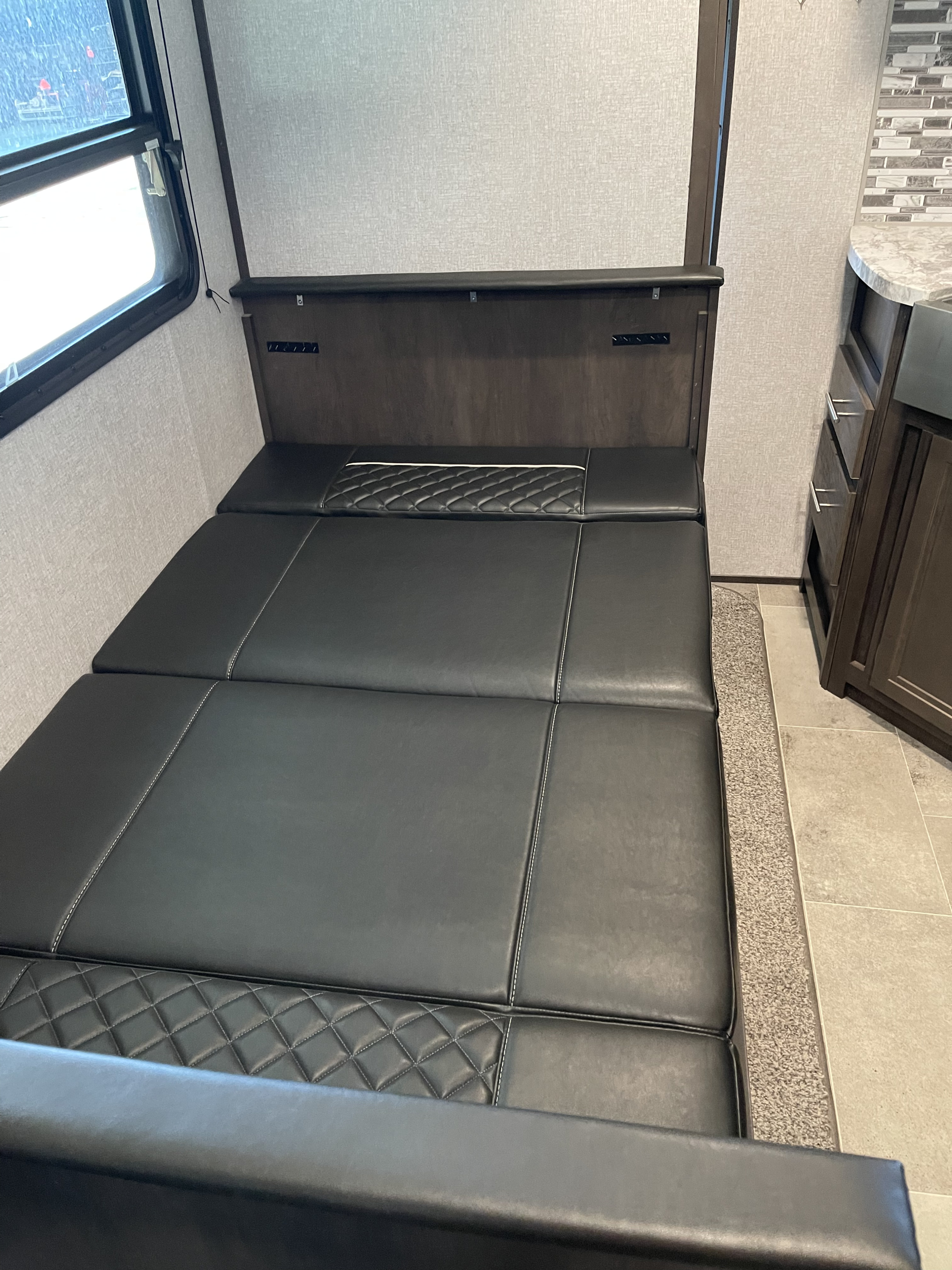 RV rental interior shows a dark leather convertible bed/sofa with diamond quilting and a compact kitchen area.. Dutchmen Other 2021