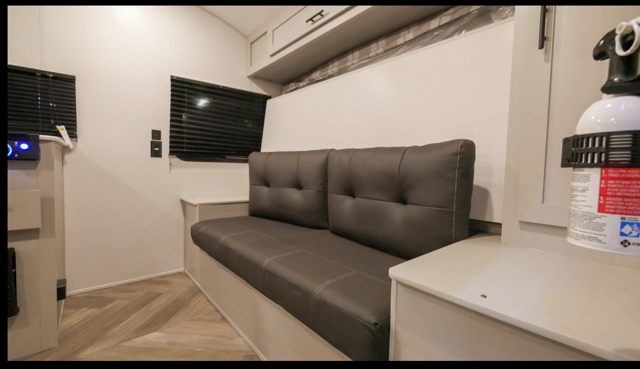 Cozy rv rental interior featuring a gray sofa, overhead storage, and a wall that conceals a murphy bed. Fire extinguisher visible.. Forest River Salem 2022