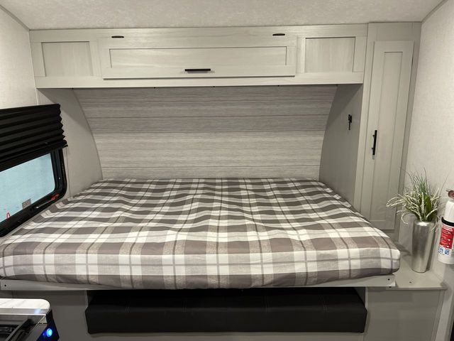 This RV rental bedroom features a comfy plaid bed, overhead cabinets, and a window with blinds, creating a cozy sleeping space.. Forest River Salem 2022