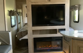 Inside a spacious RV rental showing a living area with TV, fireplace, and glimpse of the bedroom. Ideal for journeys.. Forest River Palomino Solaire 2021
