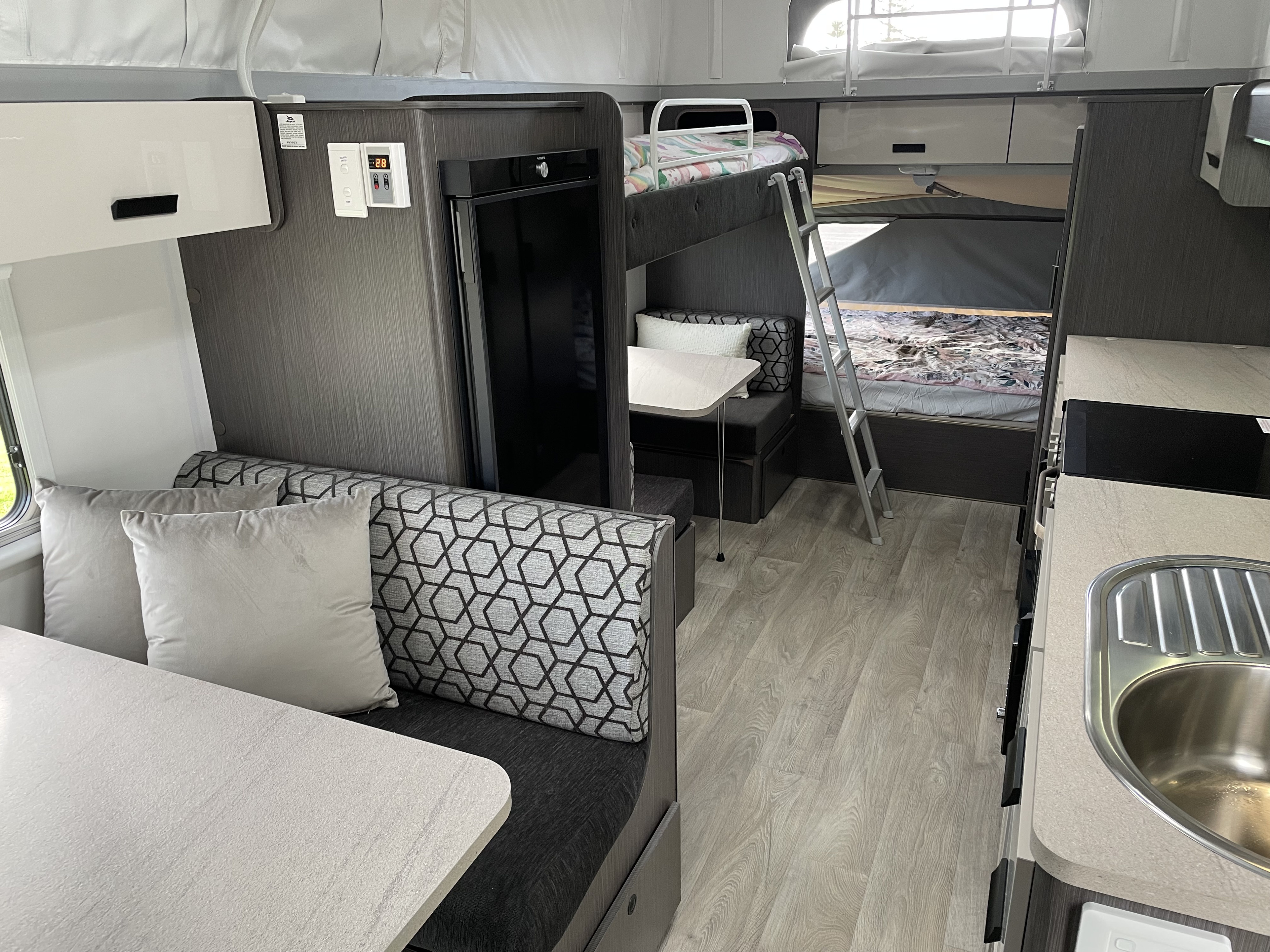 Spacious modern rv rental interior featuring a dinette, bunk beds, and compact kitchen with sink and refrigerator.. Jayco Expanda 17.56 Outback 2021